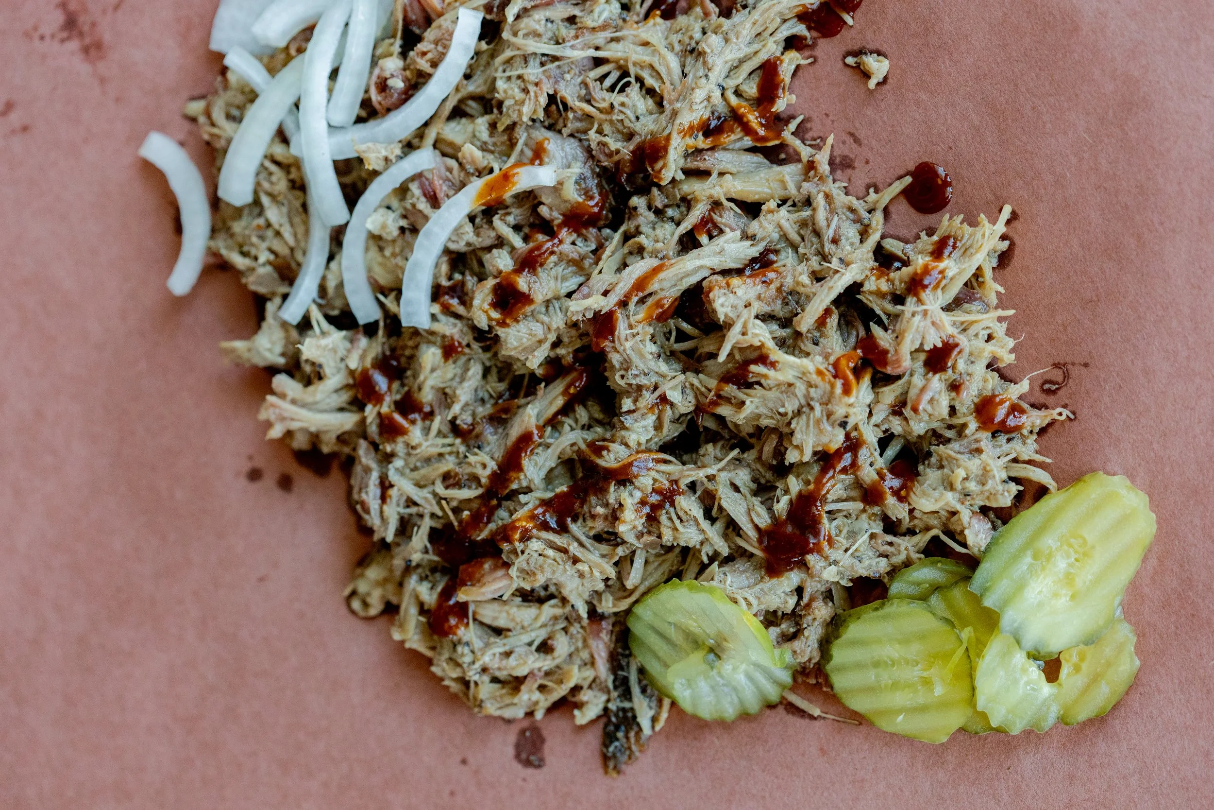  shredded barbecue chicken with barbecue sauce, served on a brown paper tray with sliced cucumbers and shredded lettuce.
