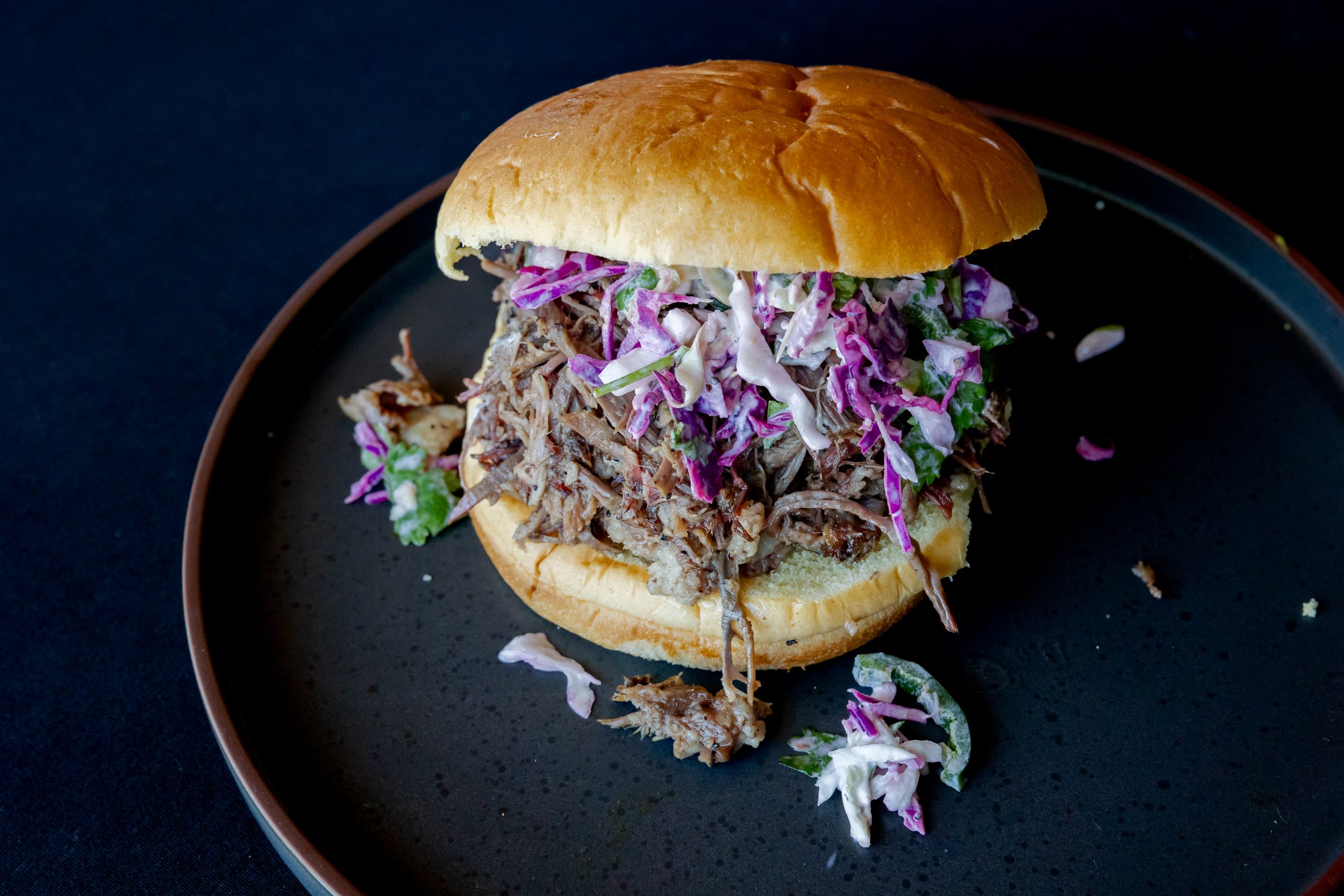 Pulled pork sandwich with coleslaw on a bun on a black plate.