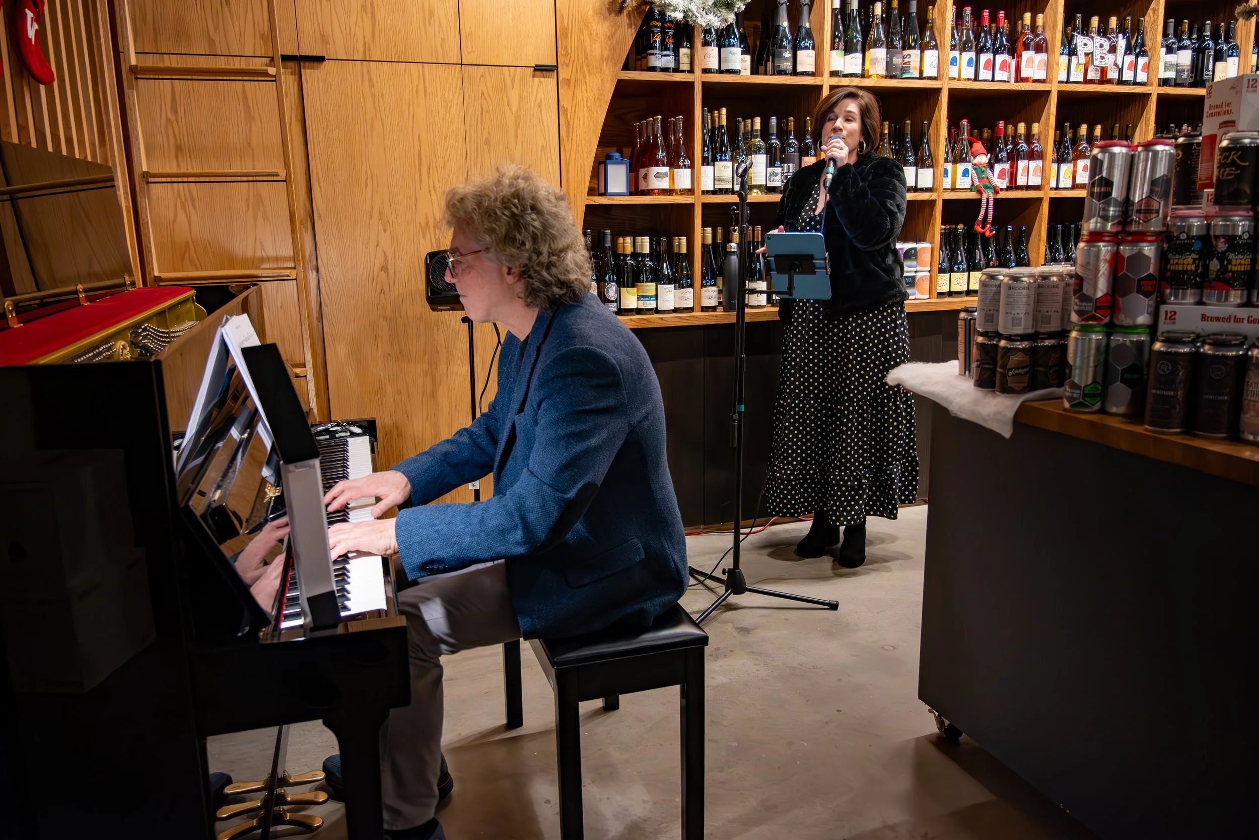Woman playing piano with another woman singing into a microphone in a store decorated for Christmas.