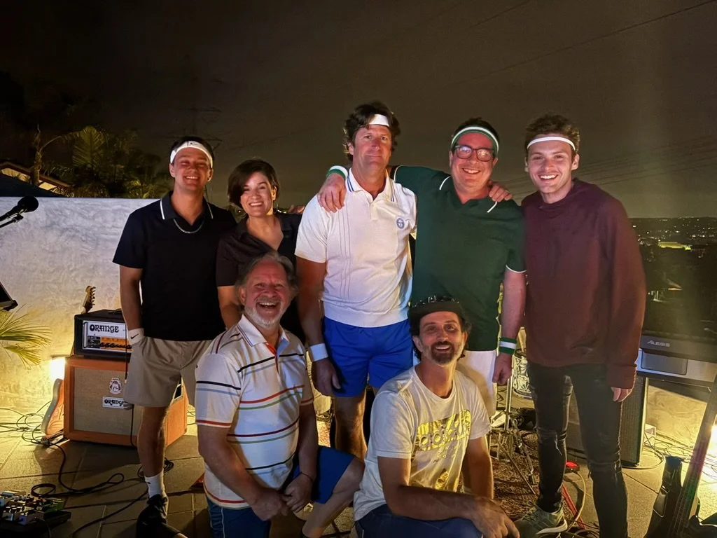Group of seven people at a rooftop party or event at night, smiling and posing.