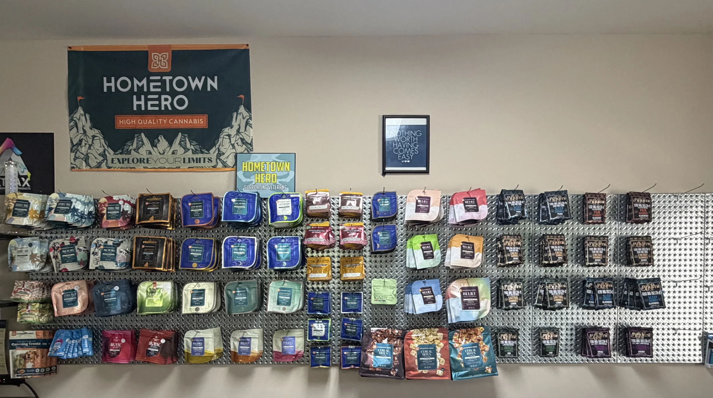 Display of various cannabis products arranged on a metal grid wall with a banner reading 'Hometown Hero' promoting high quality cannabis, and a framed quote on the wall.