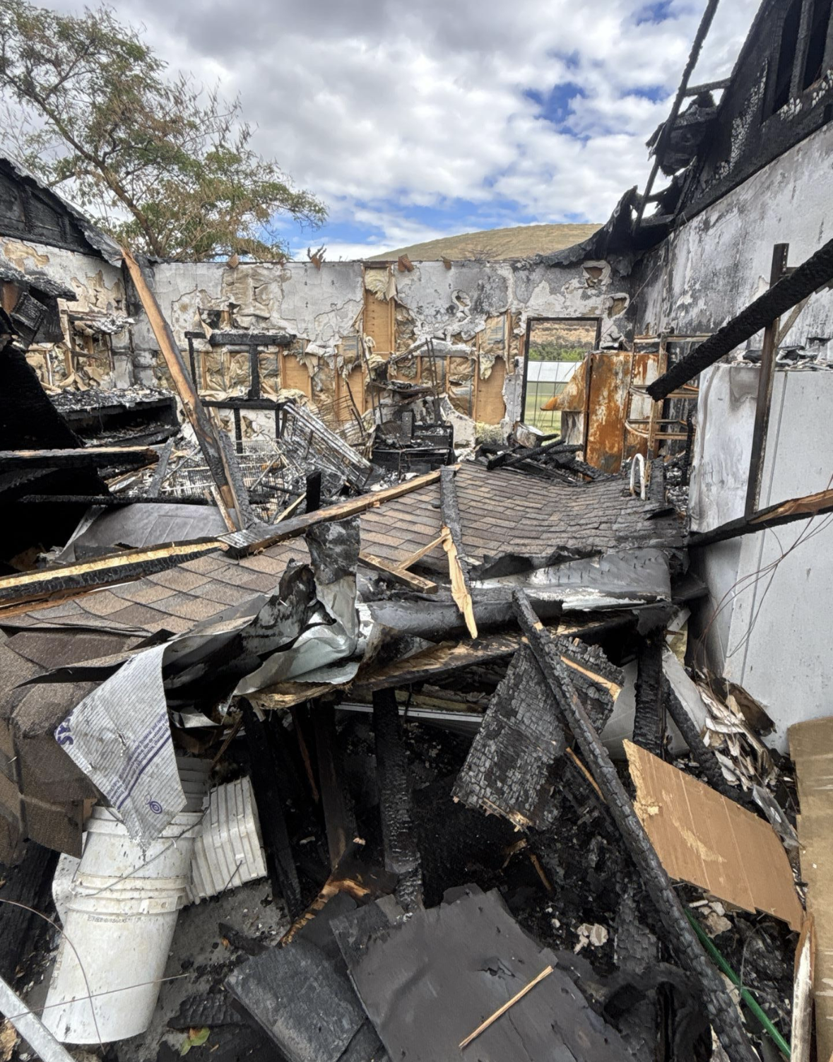 The remains of a house after a fire, with charred walls, burnt debris, and damaged furniture visible inside.