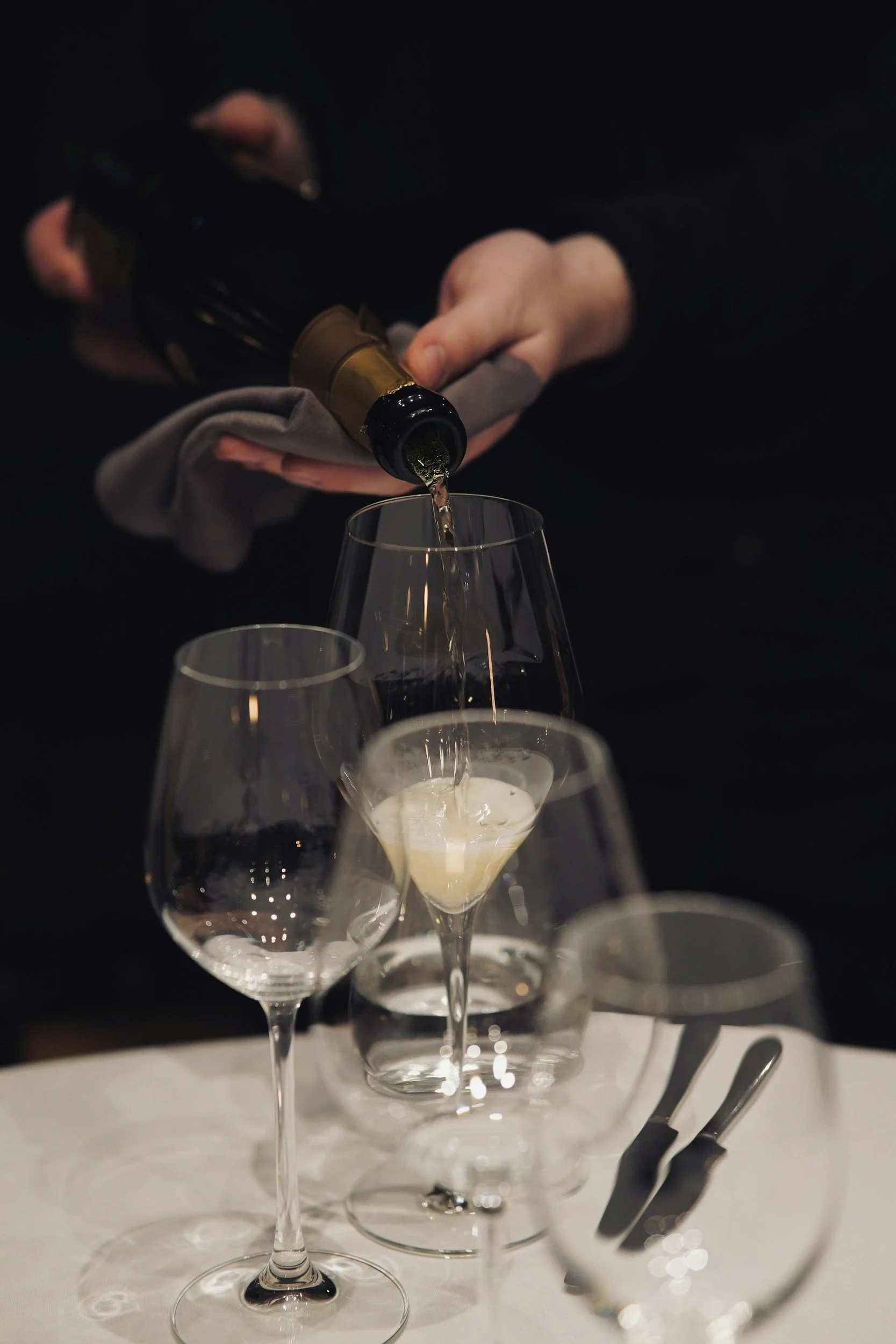 Person pouring champagne into a glass at a formal dining table.