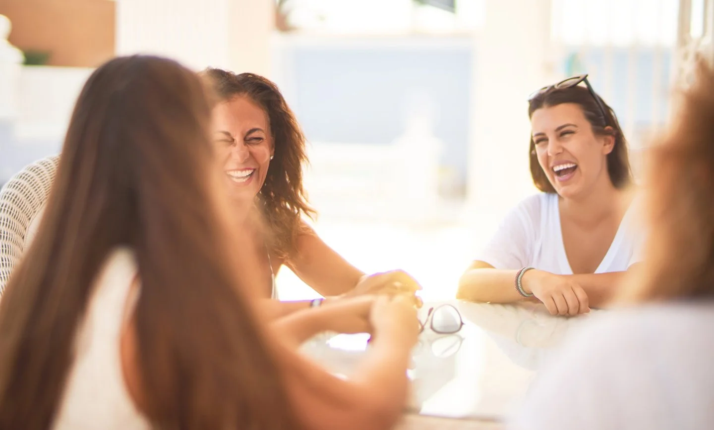 Group of women sitting at a table, laughing and enjoying conversation in a bright, sunny room.
