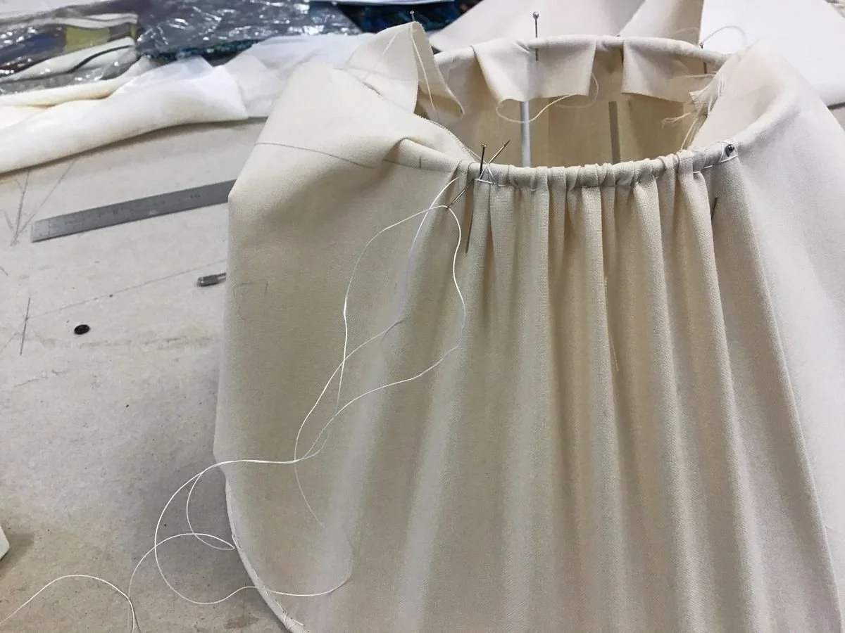 Une pièce de tissu beige en cours de couture avec des épingles et des fils, sur une table de travail.