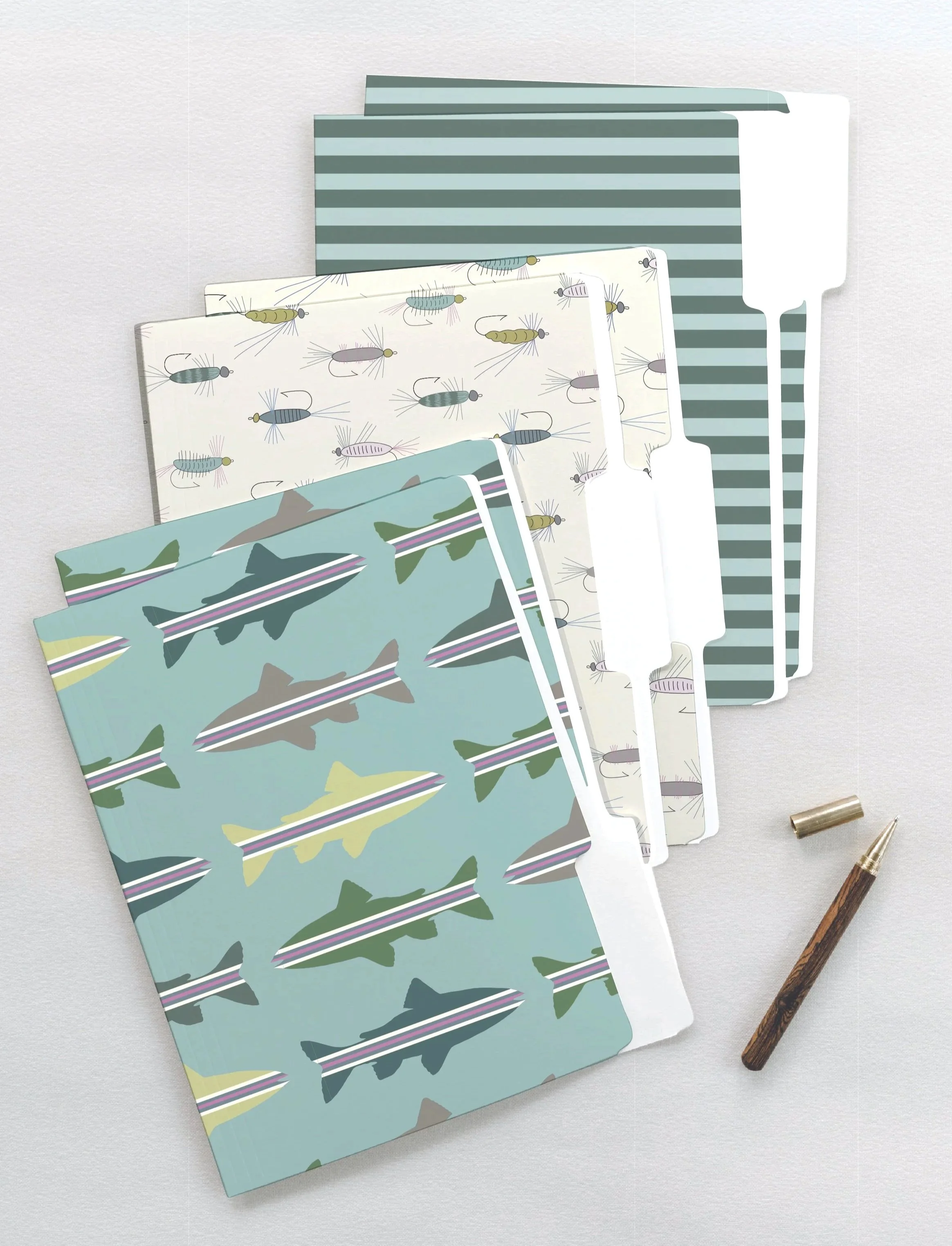 A set of patterned file folders with fish and fishing lure designs, and stripes and a pen with a wooden body, and a small metallic clip on a light-colored surface.