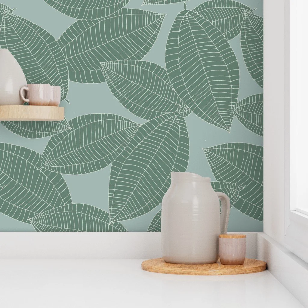 Decorative wallpaper with large green leaf pattern, white pitcher, and small mug on a circular wooden tray in front of a window.