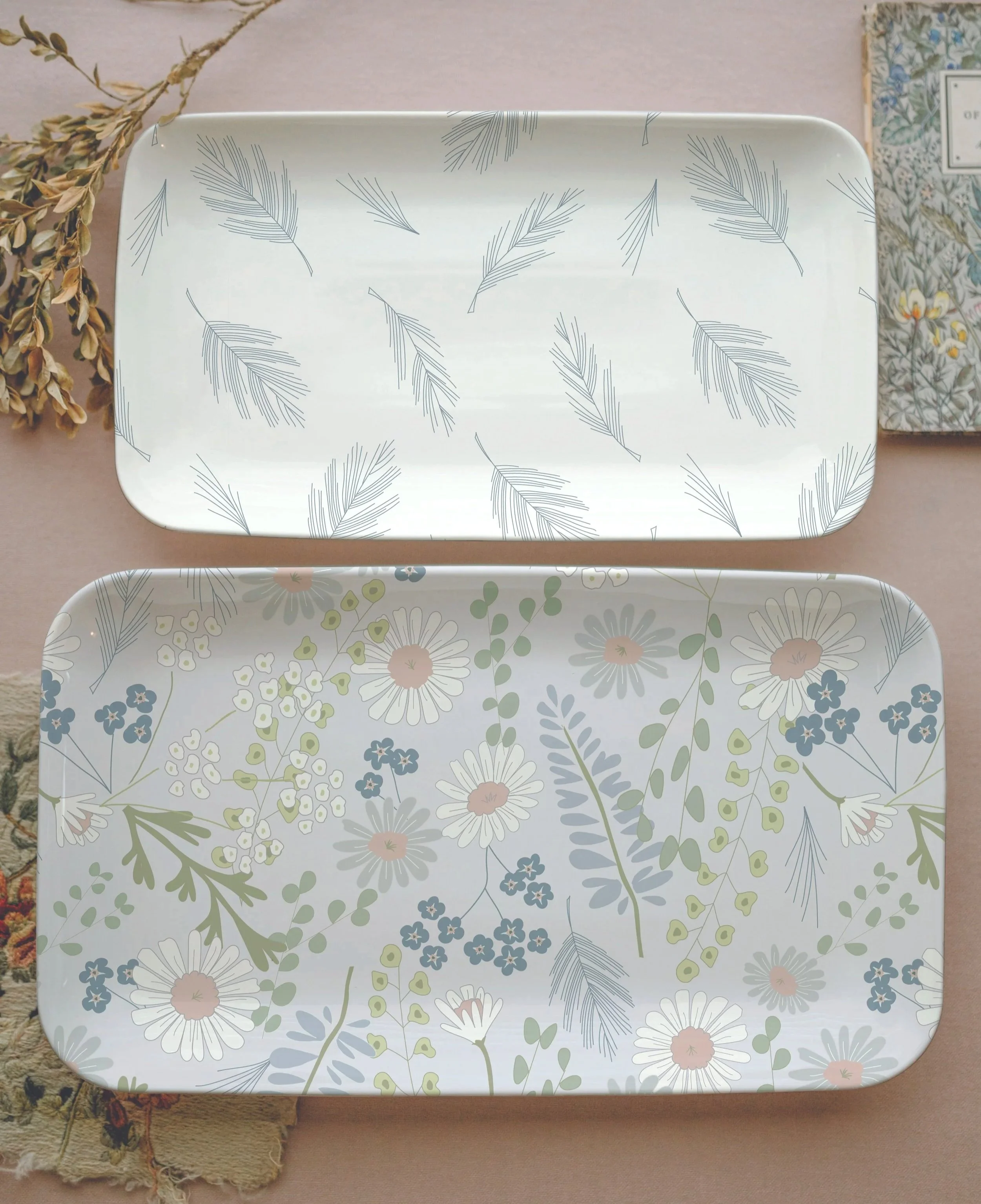 Two rectangular trays with floral designs, one with a white background and a pattern of light blue, green, and pink flowers and leaves, the other with a white background and a pattern of blue, green, and pink flowers and leaves.