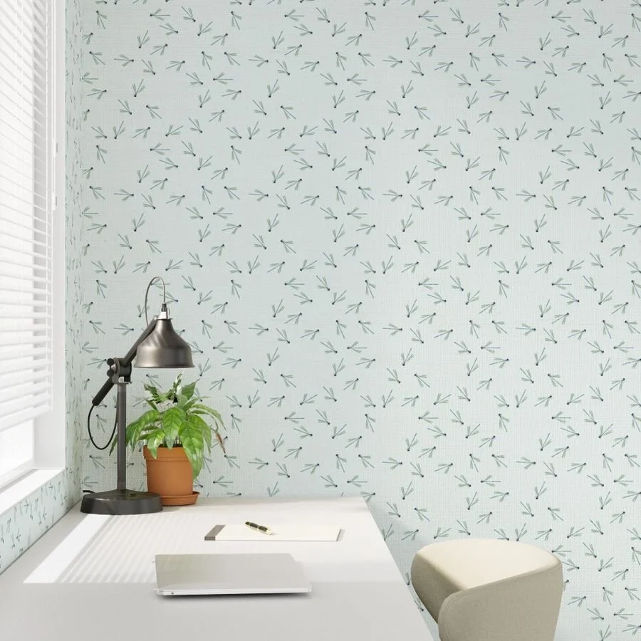 A home office desk setup with a white desk, a black desk lamp, a potted green plant, and a white cushioned chair, against a wallpapered wall with a pattern of scattered dragonflies.