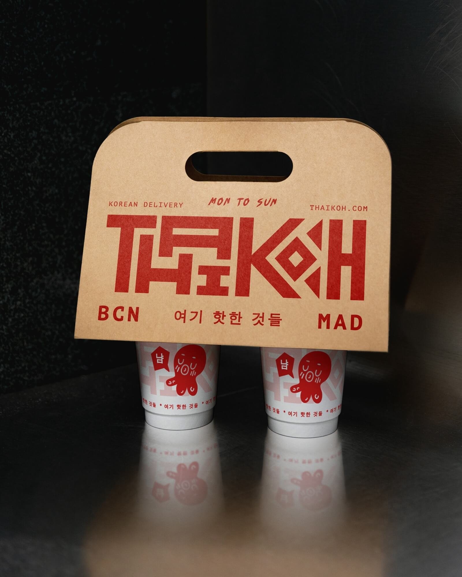 Caja de comida para llevar de ThaiKoh, con ilustración de un pulpo rojo en cada vaso. Texto en la caja en inglés y coreano, con información de entrega y localizaciones.