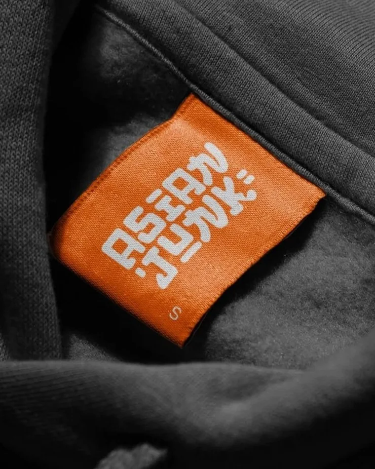 Etiqueta naranja con la marca "Asian Junk" en letras blancas en la ropa de color gris.