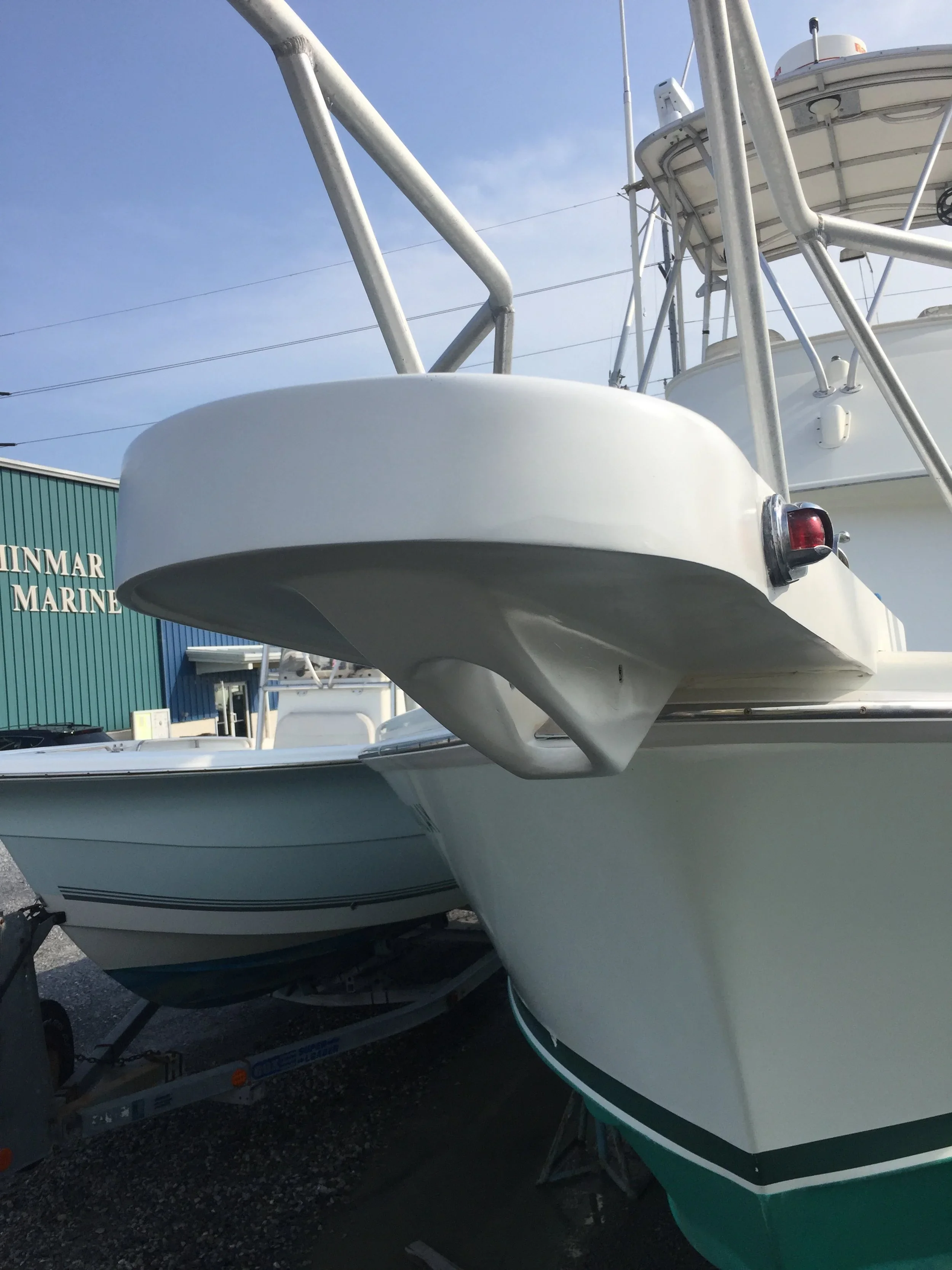Two white boats on trailers parked outdoors near a green building with the words 'INMAR MARINE' and a blue sky with some clouds.