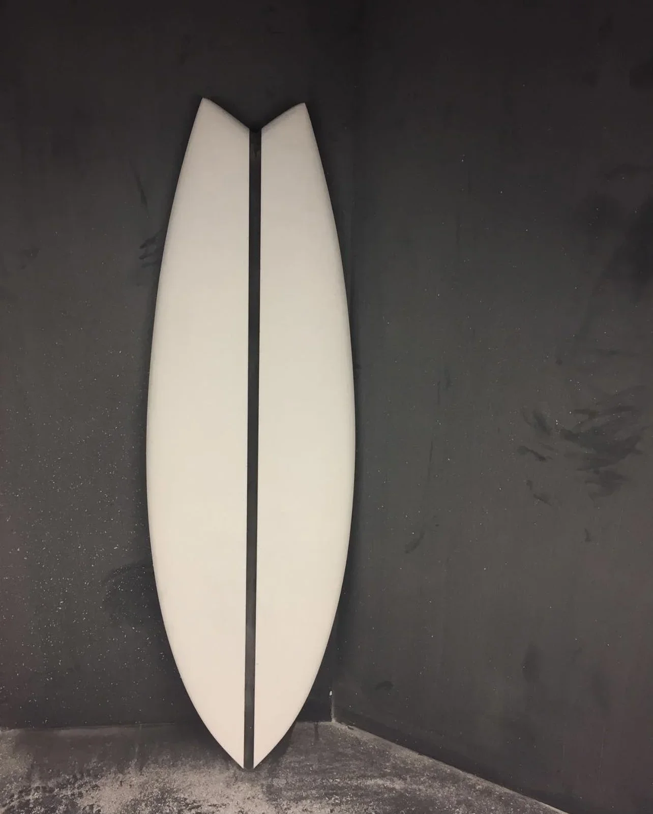 A surfboard white in color with black strip down the middle, leaning vertically against a dark wall.