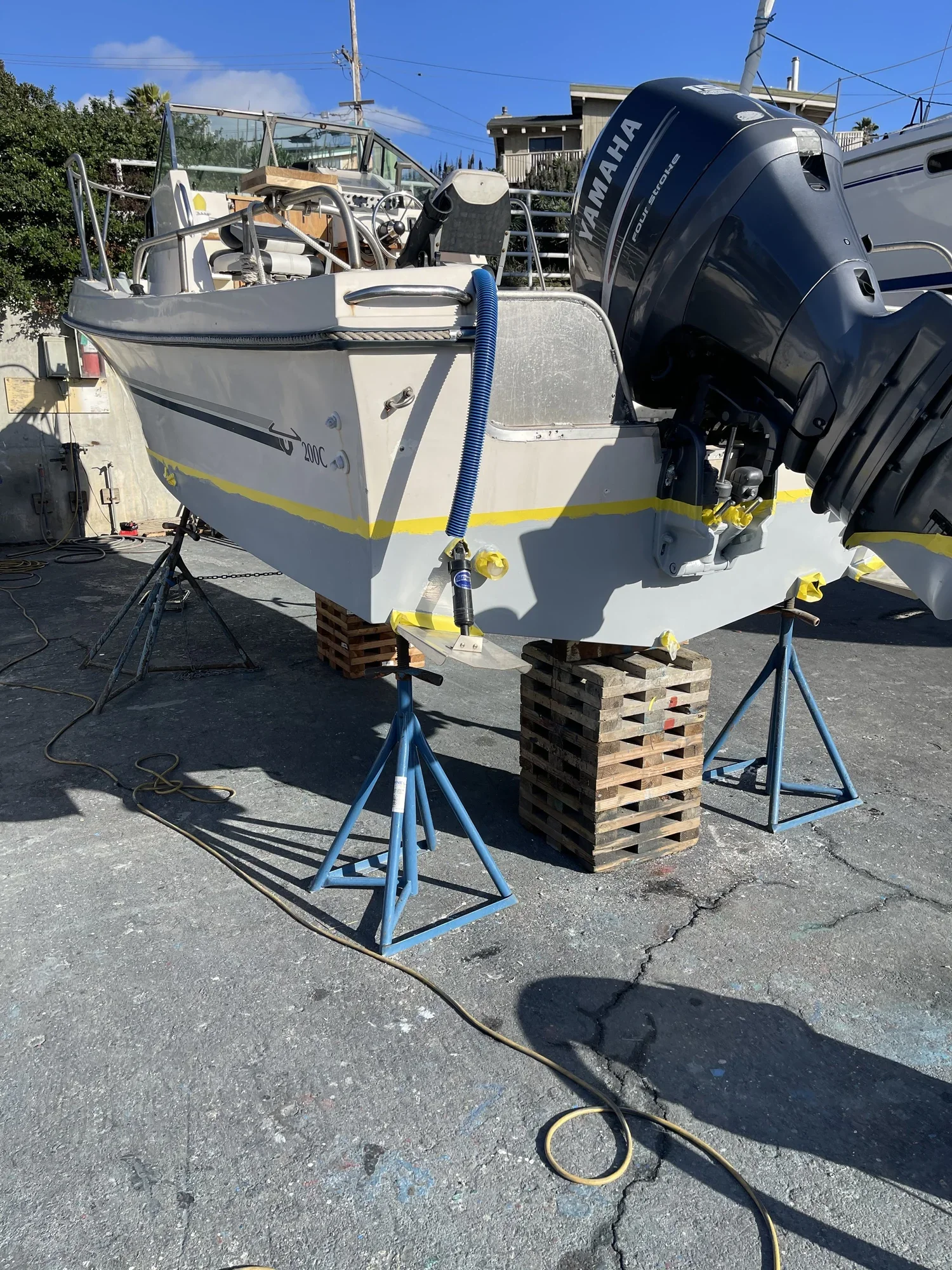 A boat with a Yamaha engine on a trailer in an outdoor lot, supported by wooden blocks and blue stands, with yellow tape marking the bottom edge.