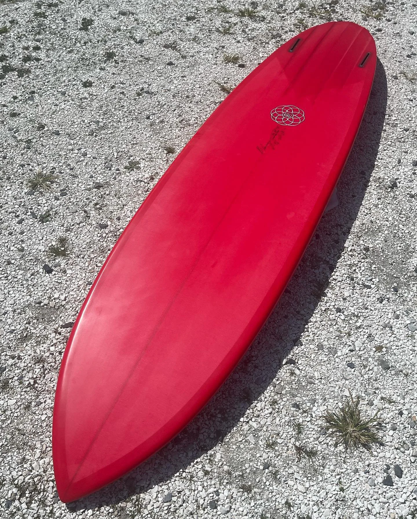 Red surfboard lying on rocky ground.