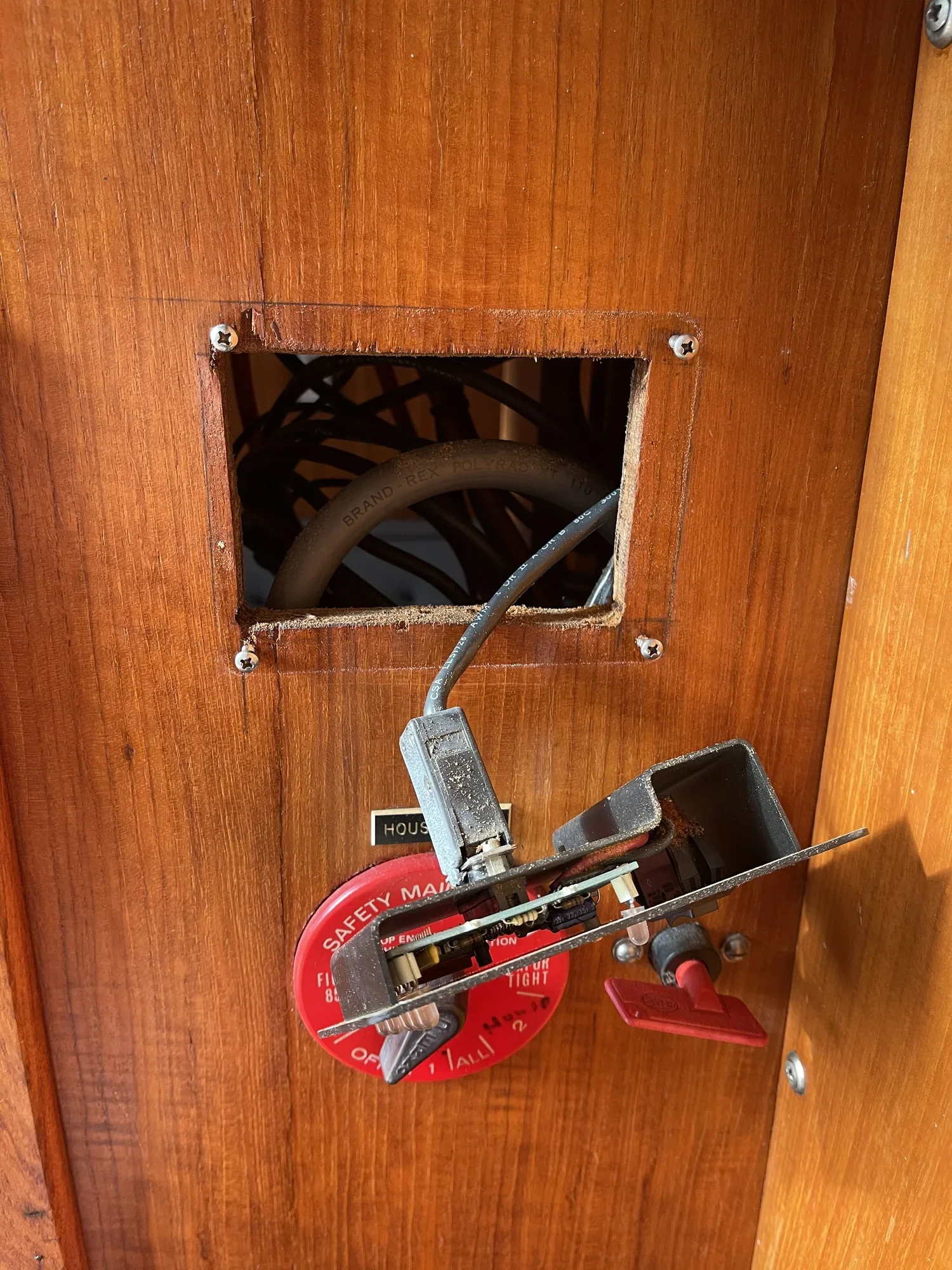 Electrical wiring behind a wooden panel, with a voltage tester and fire safety equipment nearby.