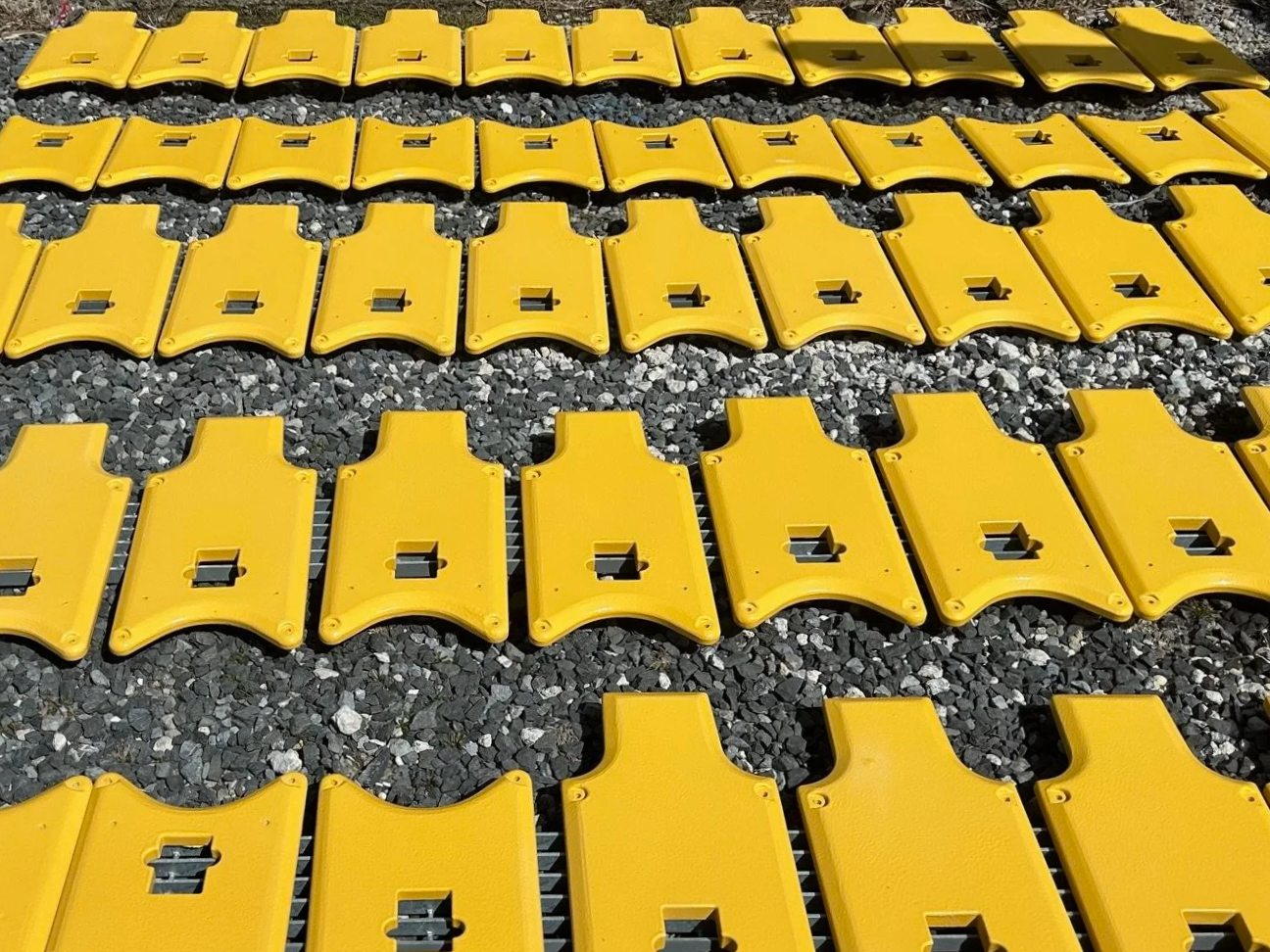 Multiple yellow plastic connectors with metal hooks lying on a gravel surface, arranged in rows.