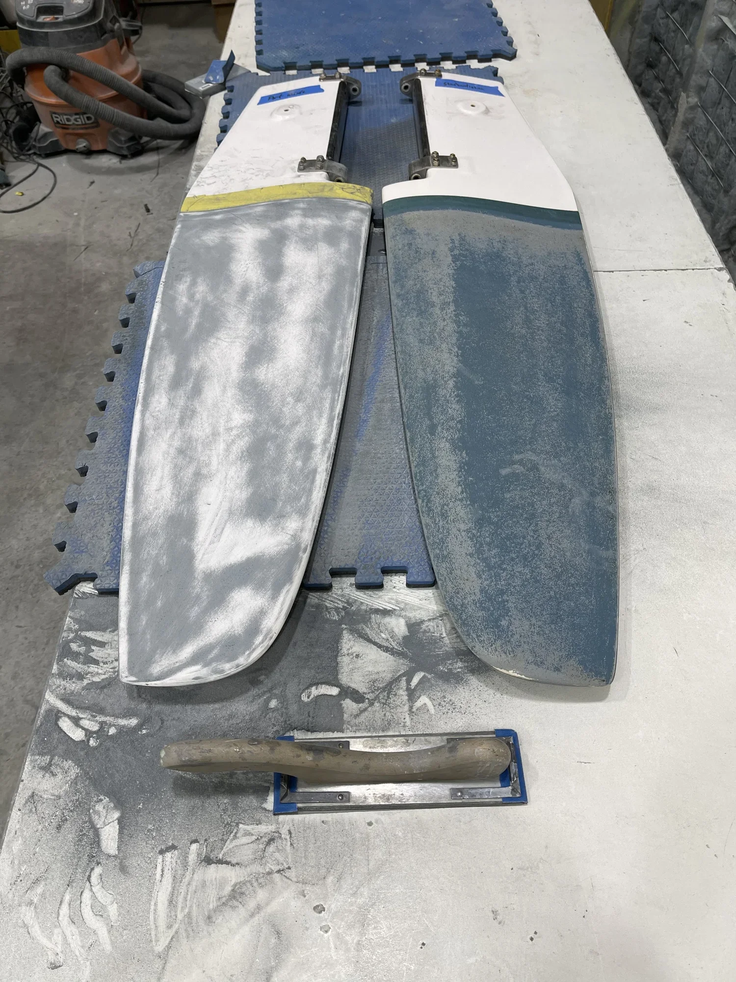 Two large sanding blocks with a metallic surface, one partially sanded and the other more worn, placed on a workbench in a workshop.