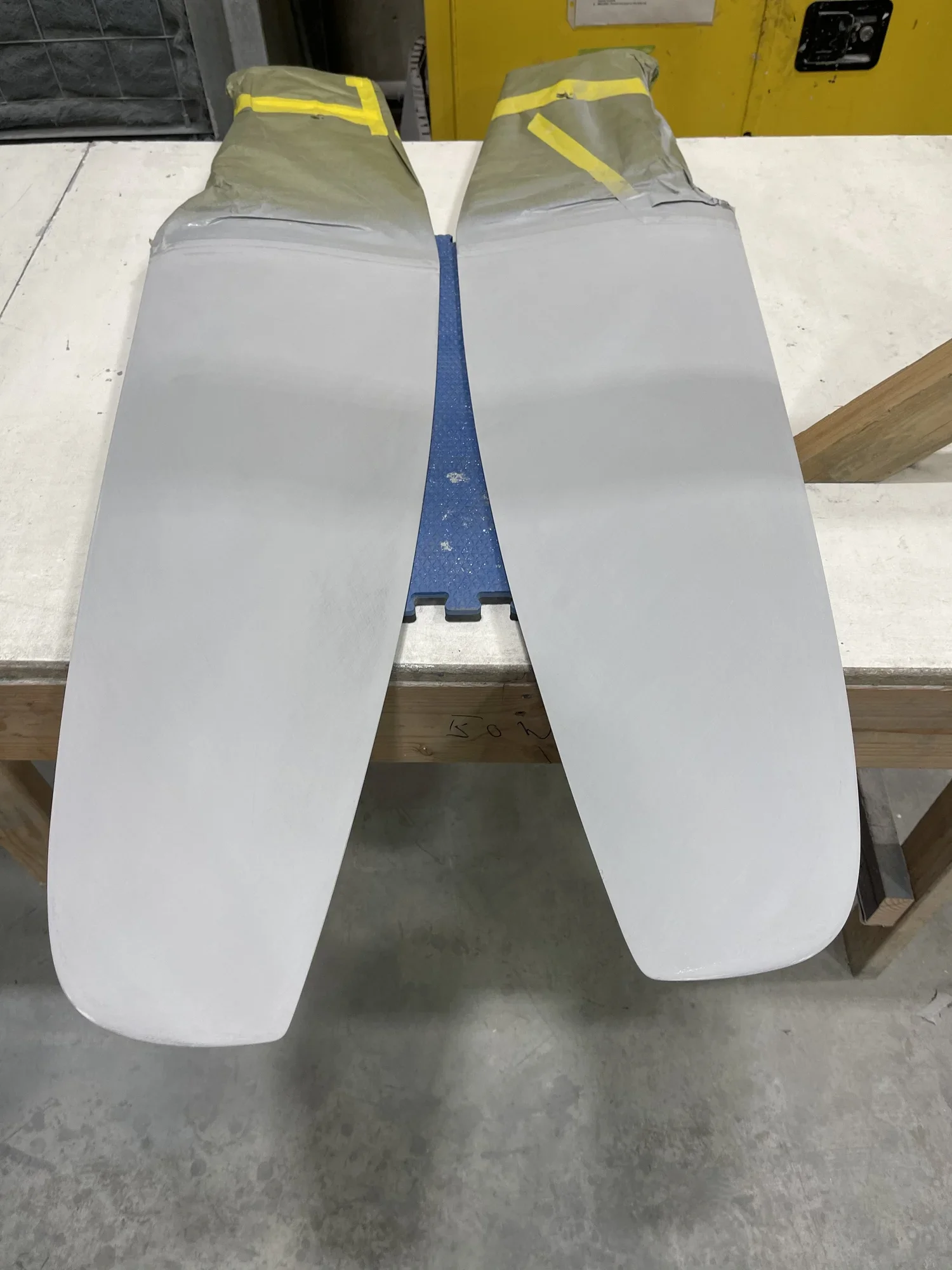 Two large white fiberglass skis with rounded tips resting on a workbench in a workshop.