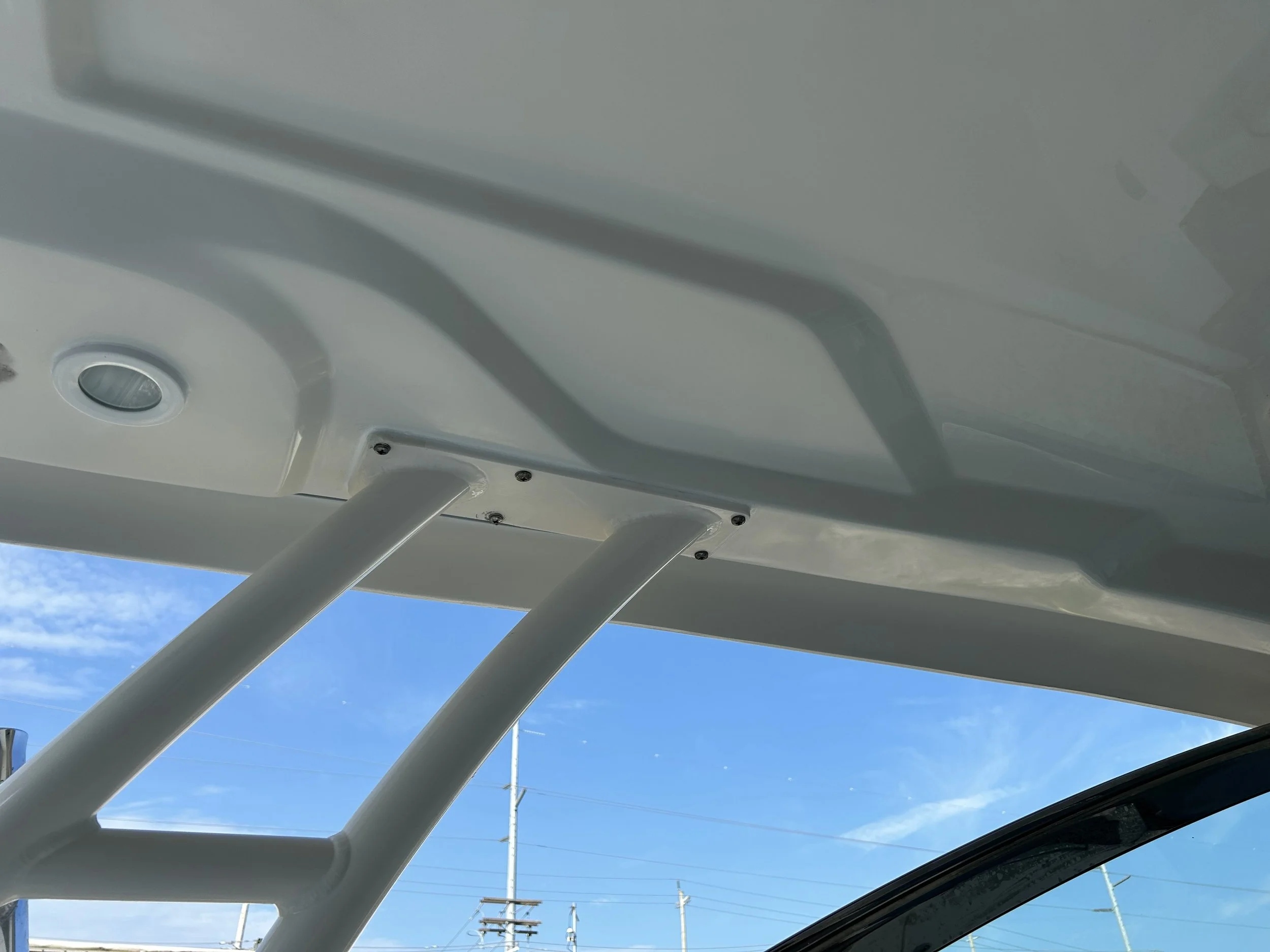 Looking up at a white boat canopy with metal support bars against a blue sky with some clouds and power lines in the background. Finished gelcoat repair