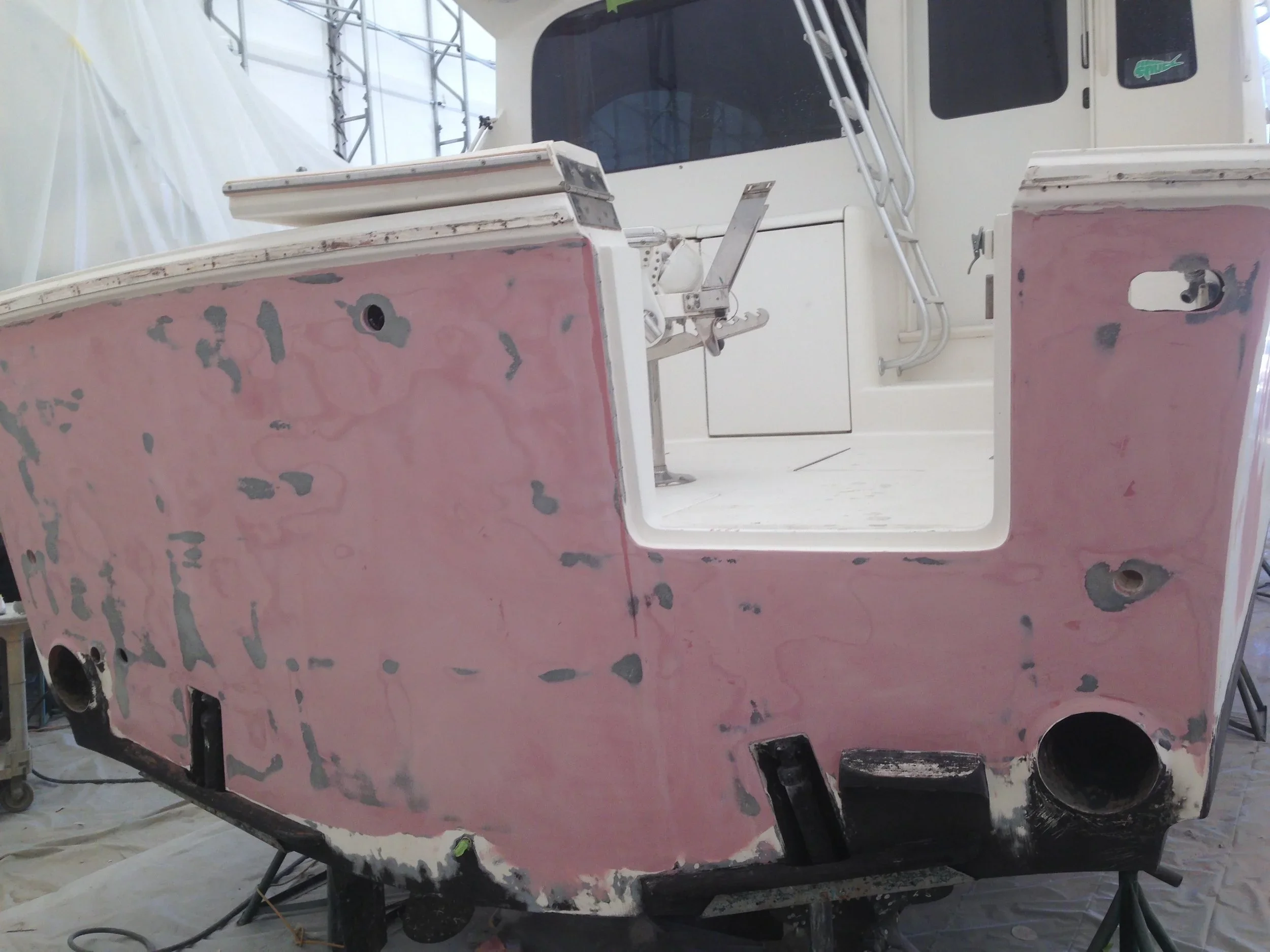 The image shows a boat with pink and black painted hulls, undergoing restoration inside a workshop. The boat's interior and exterior are visible, with some parts not yet painted.