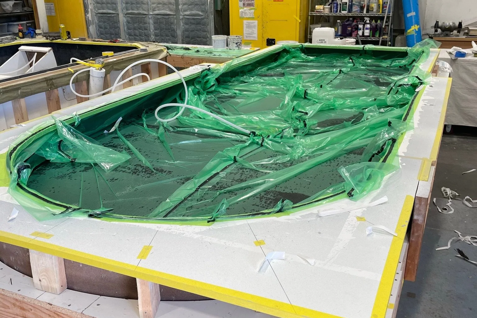 A mold for a hovercraft being constructed in a workshop, with green plastic covering and masking tape around the edges, surrounded by tools and materials.