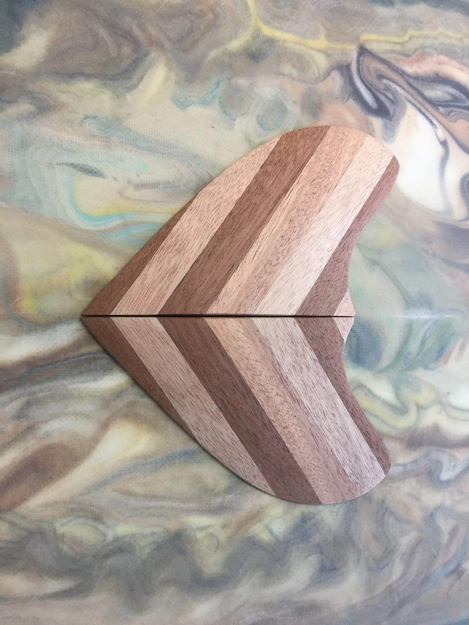A wooden geometric object with a chevron pattern, placed on a multicolored, marbled, fabric surface.
