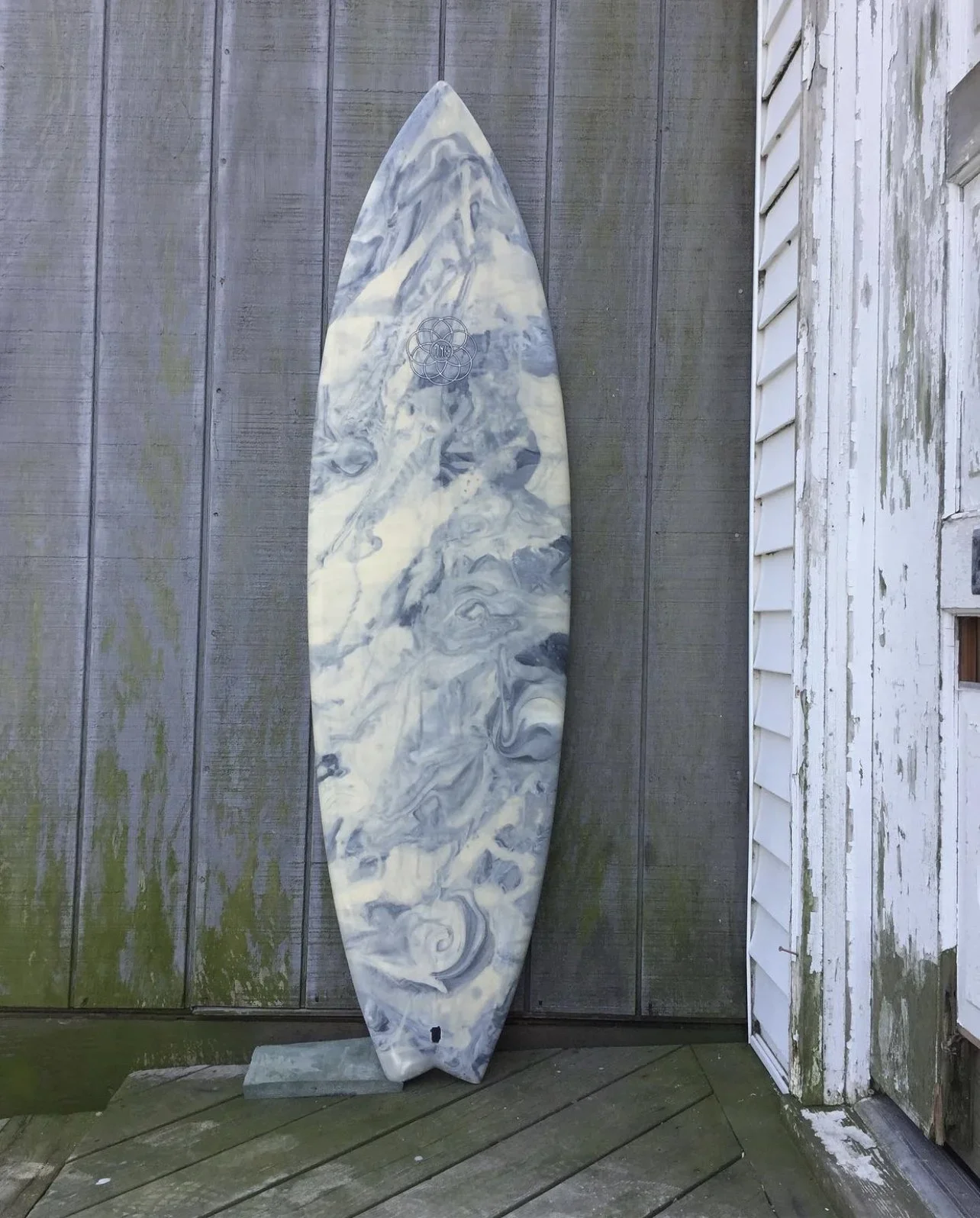 Marbled surfboard leaning against weathered wooden fence next to white weathered house siding.