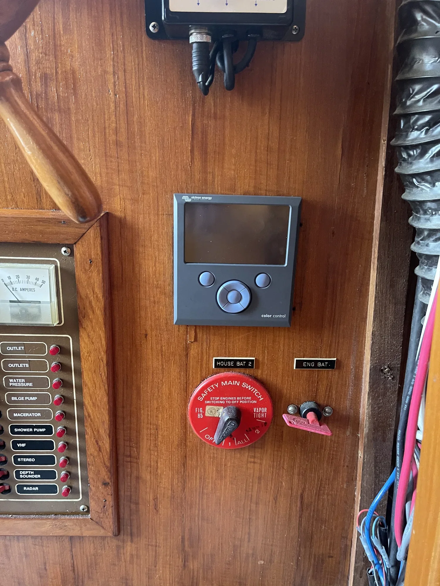 A wooden control panel with switches, gauges, and electronic devices including a digital display labeled 'Color Control.' There are labels for 'House Bat 2' and 'Eng Bat.' A red safety main switch is also visible with instructions to stop engines before switching to off position, along with various wiring and cables.