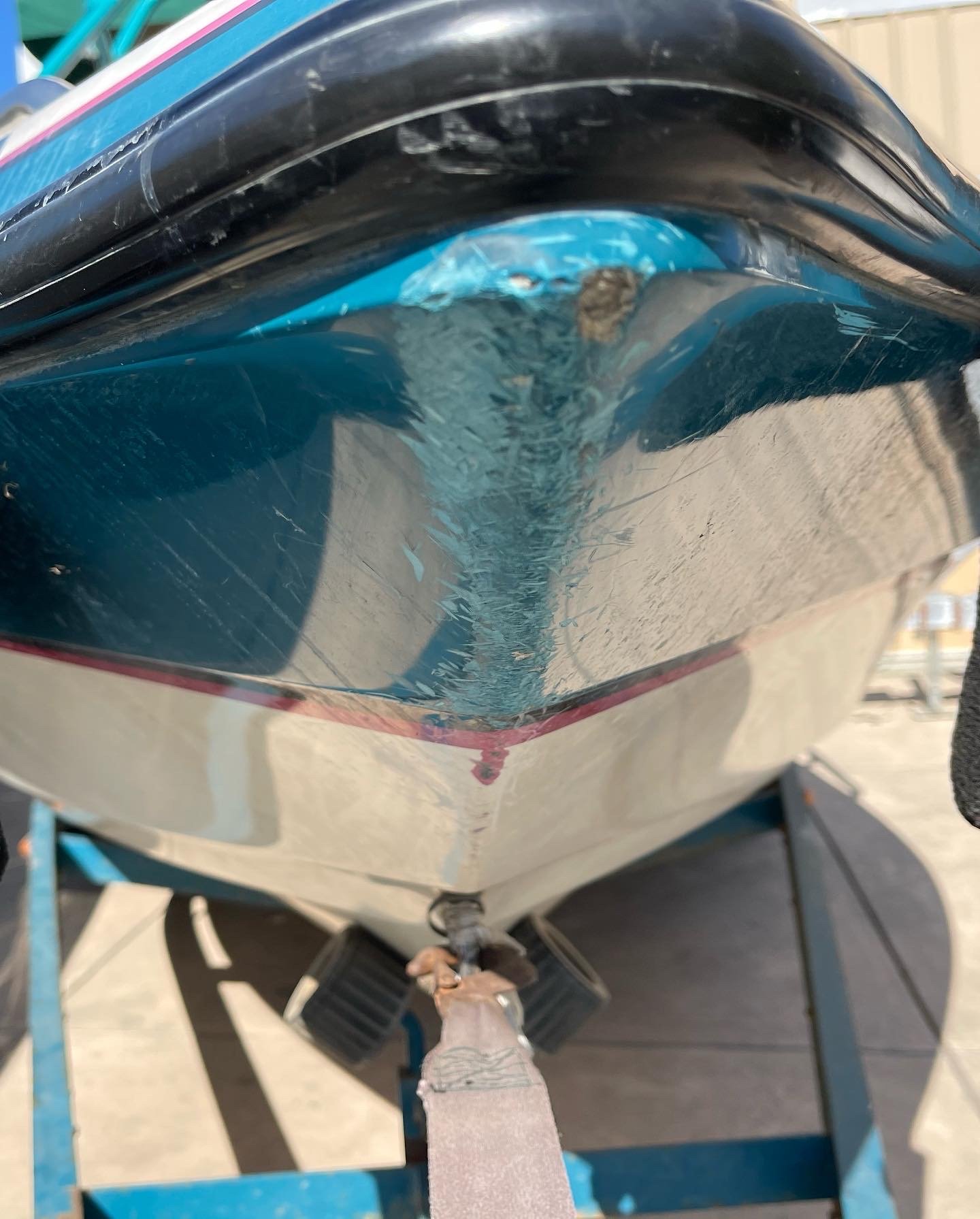 Close-up of a boat's bow showing a cracked or damaged section, mounted on a blue stand, needing gelcoat repair.