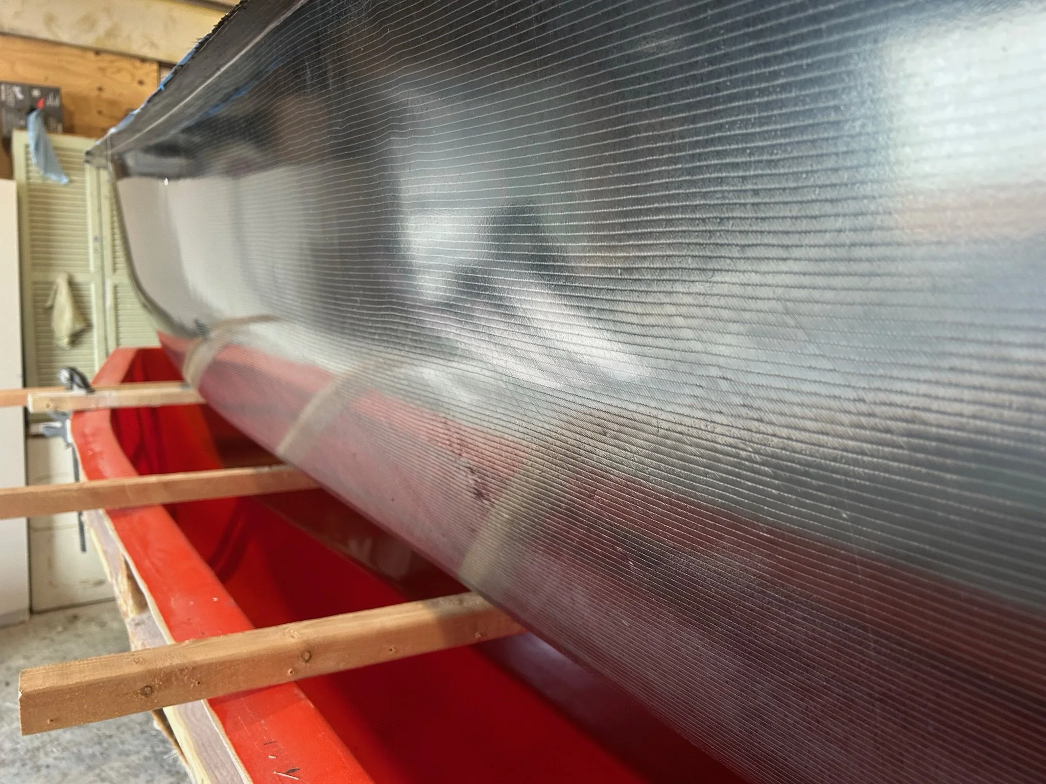 A carbon fiber surface with thin horizontal grooves, supported by a red and wooden frame, in a workshop or garage setting.