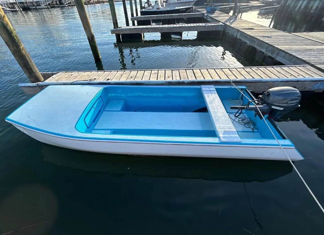 A small blue and white motorboat moored at a wooden dock on calm water.