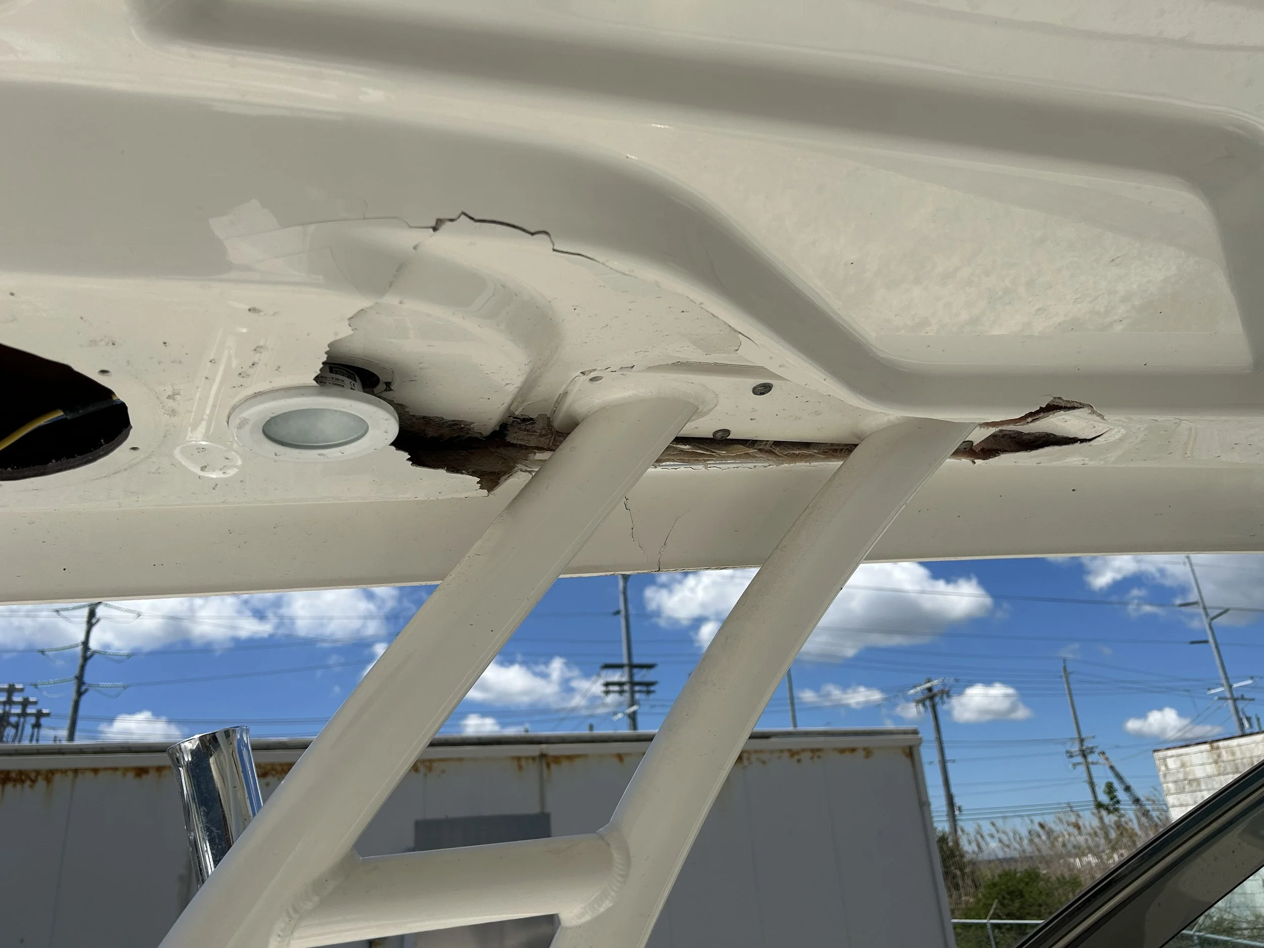 Close-up of a damaged white boat hull with cracks and peeling paint, set against a partly cloudy sky and power lines.