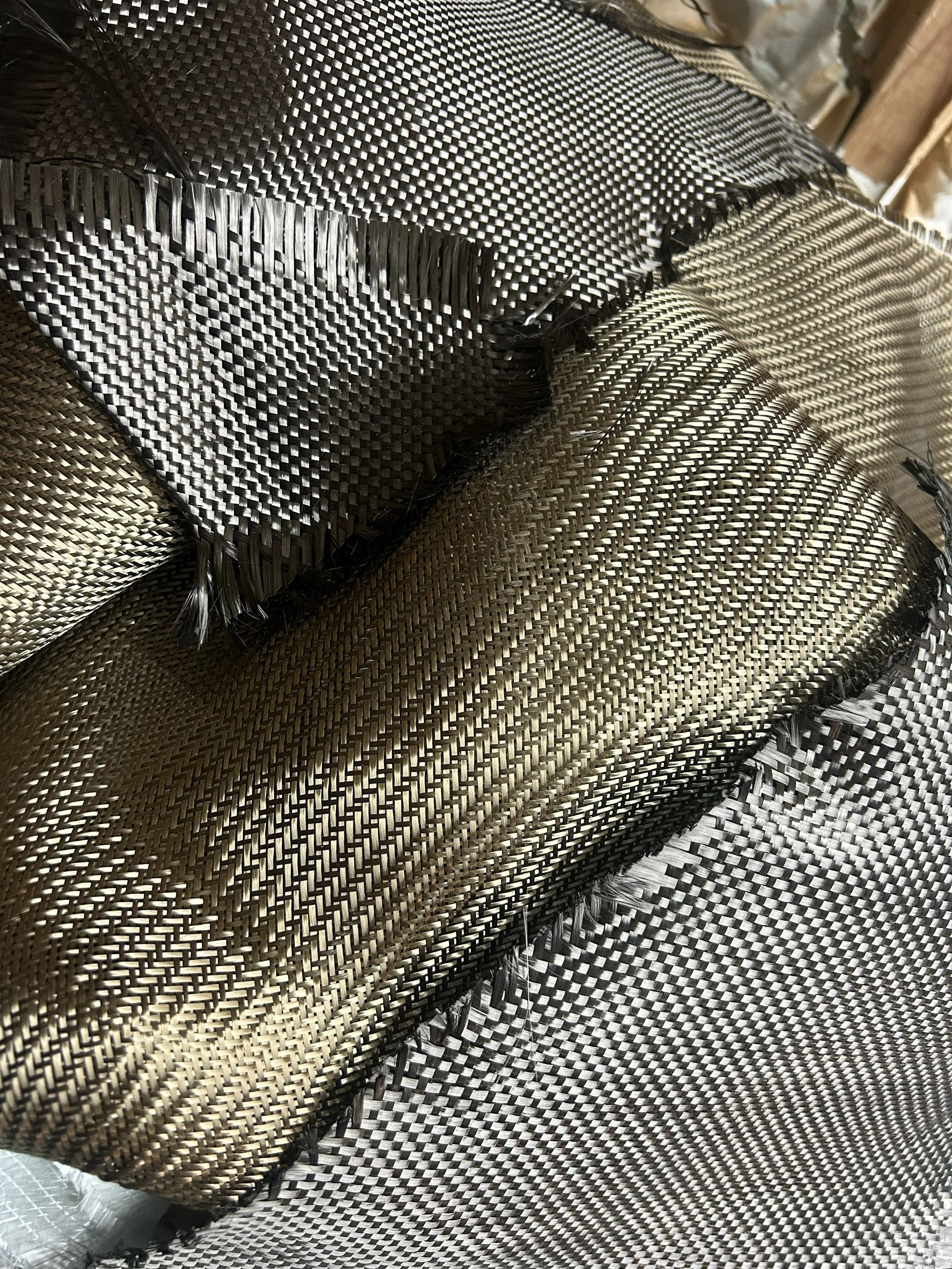 Close-up of woven carbon fiber and basalt material, possibly part of a sports car or high-performance equipment, with metallic and black fibers interlaced.