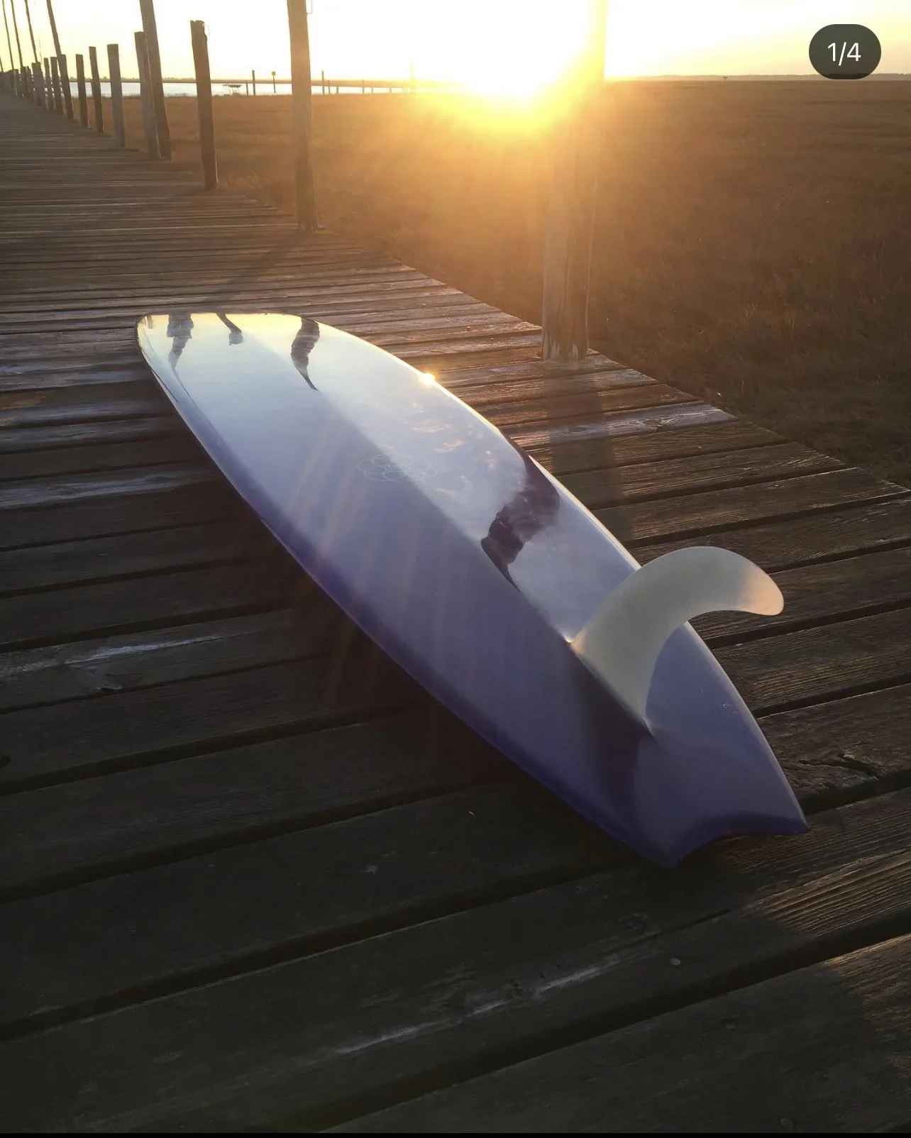 A surfboard lying on a wooden pier during sunset, with the sun shining brightly on the horizon and casting reflections on the surfboard.