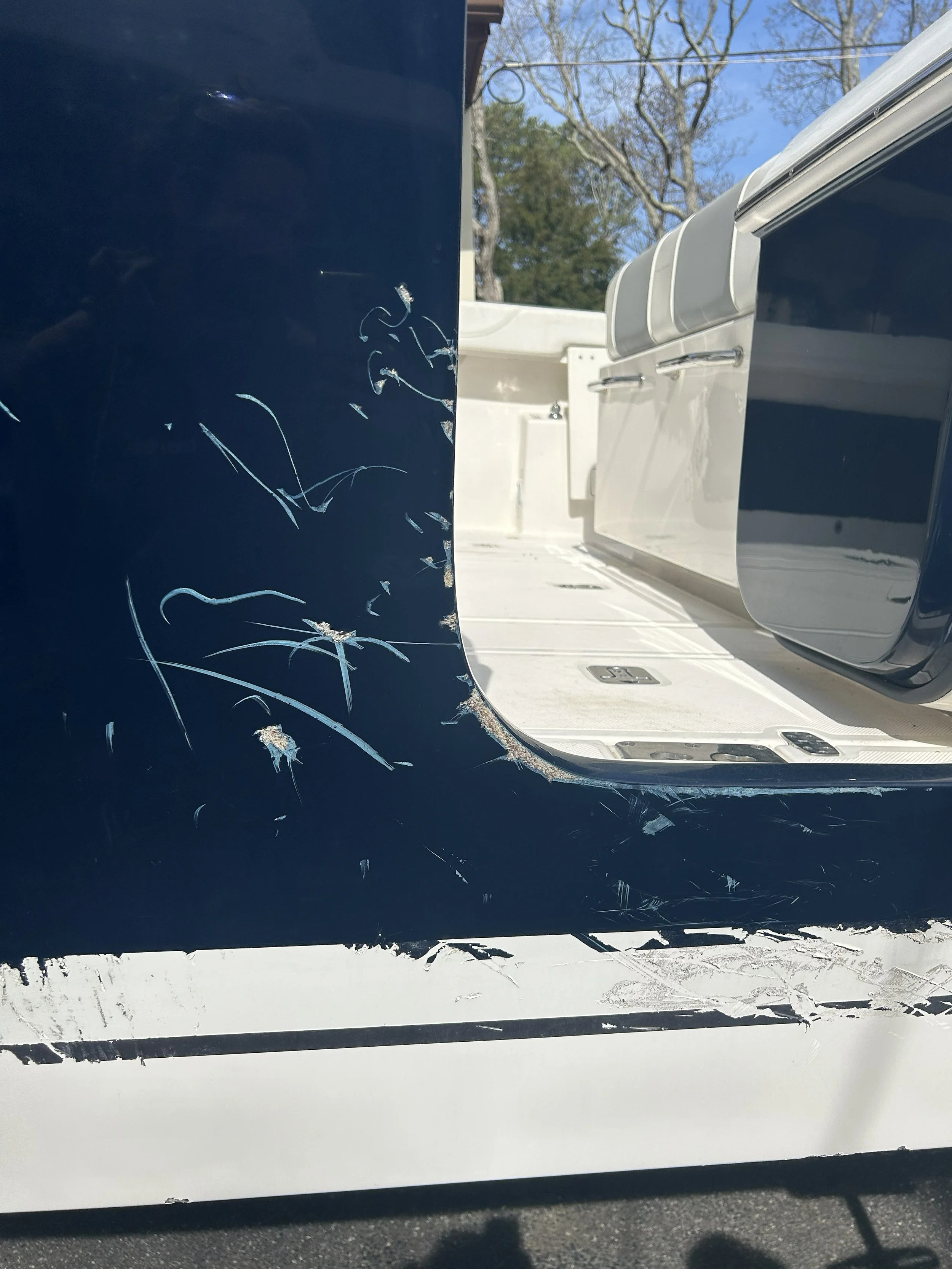 Close-up of a boat hull with white and blue paint, showing numerous scratches and scuffs on the blue section.