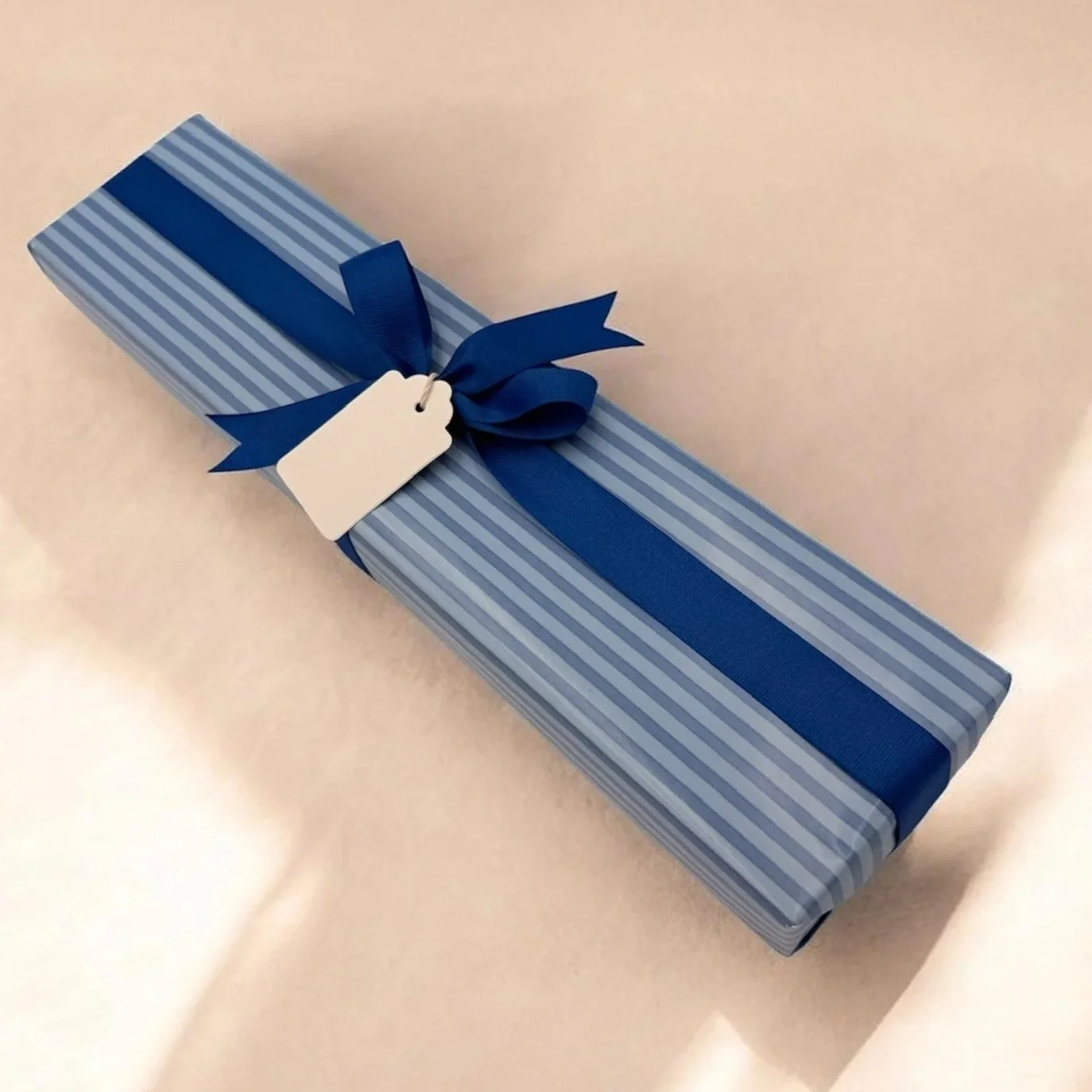 A rectangular gift box wrapped in light blue and dark blue striped paper, tied with a dark blue ribbon in a bow, with a blank white gift tag attached.