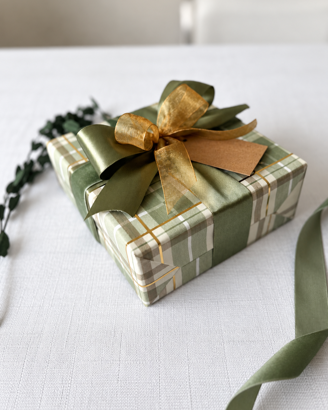Green plaid gift with layered green and gold bows and a white tag.