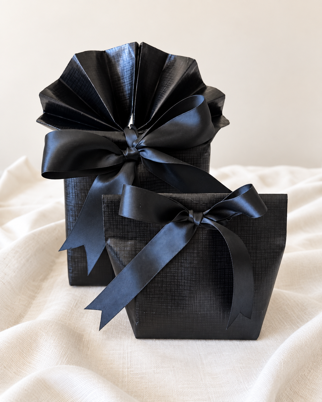 Two black gifts finished with a gathered paper top and a black ribbon bow.