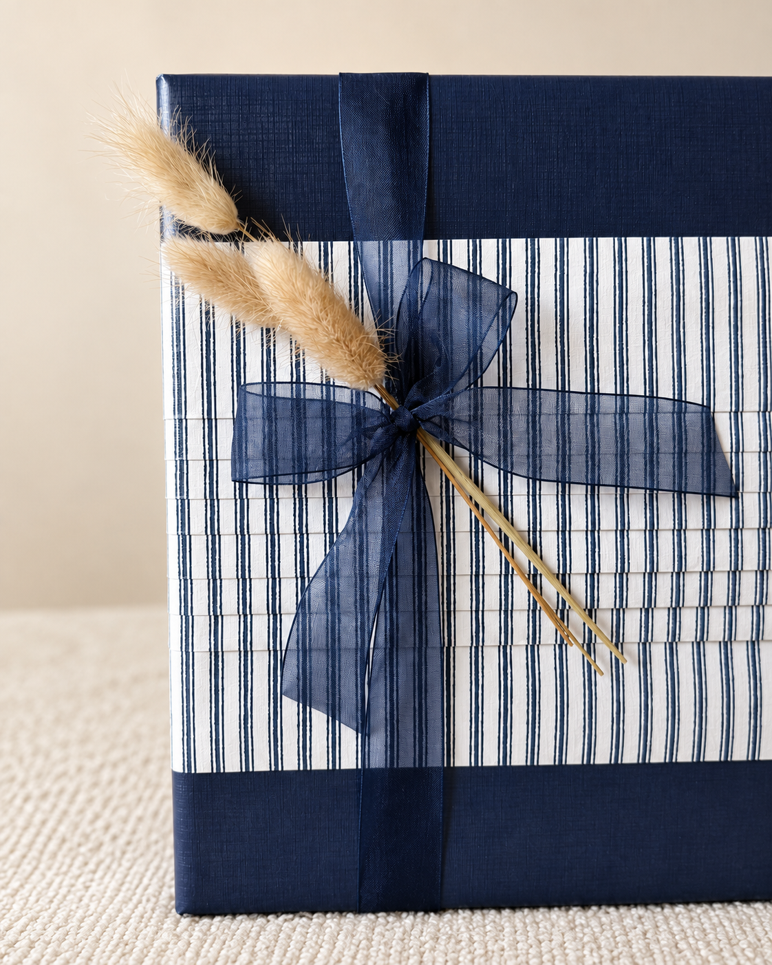 Close-up of navy striped gift wrap with a blue bow and dried grasses.