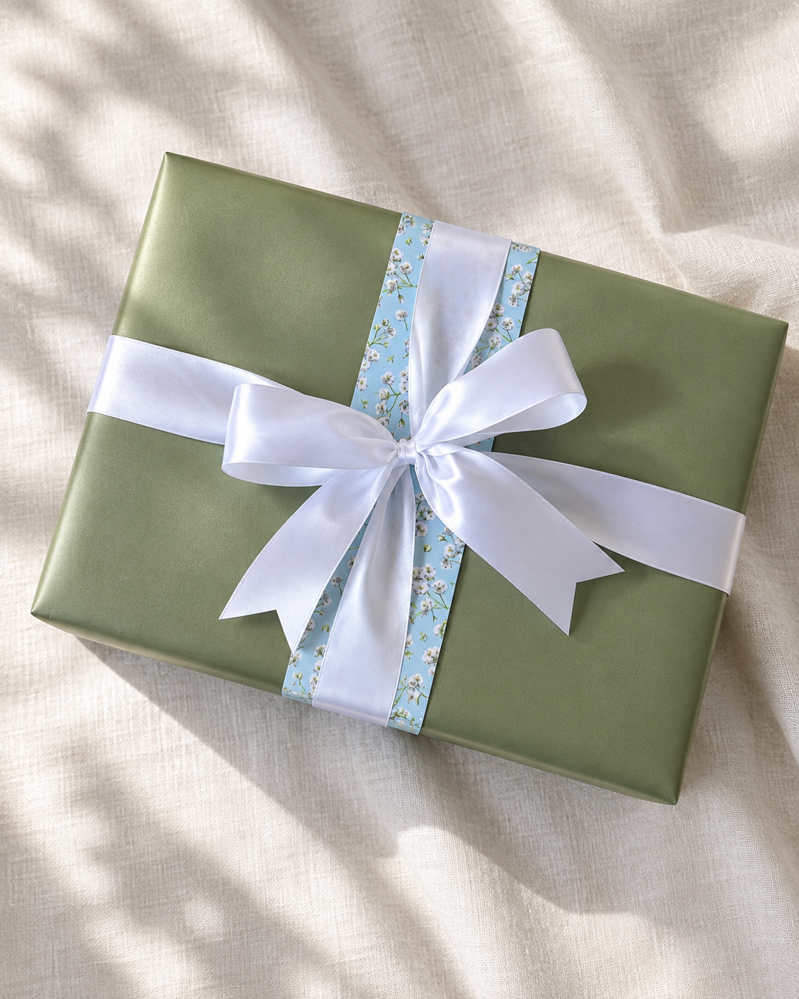 Sage green gift with a white bow and a narrow floral ribbon.