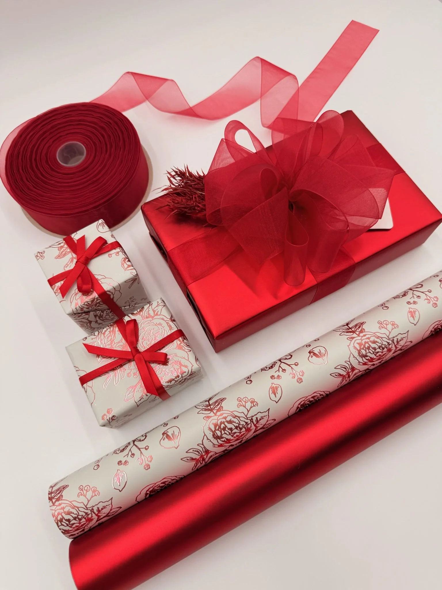 A collection of red and white wrapped gifts with ribbons, ribbons, and wrapping paper on a white surface.