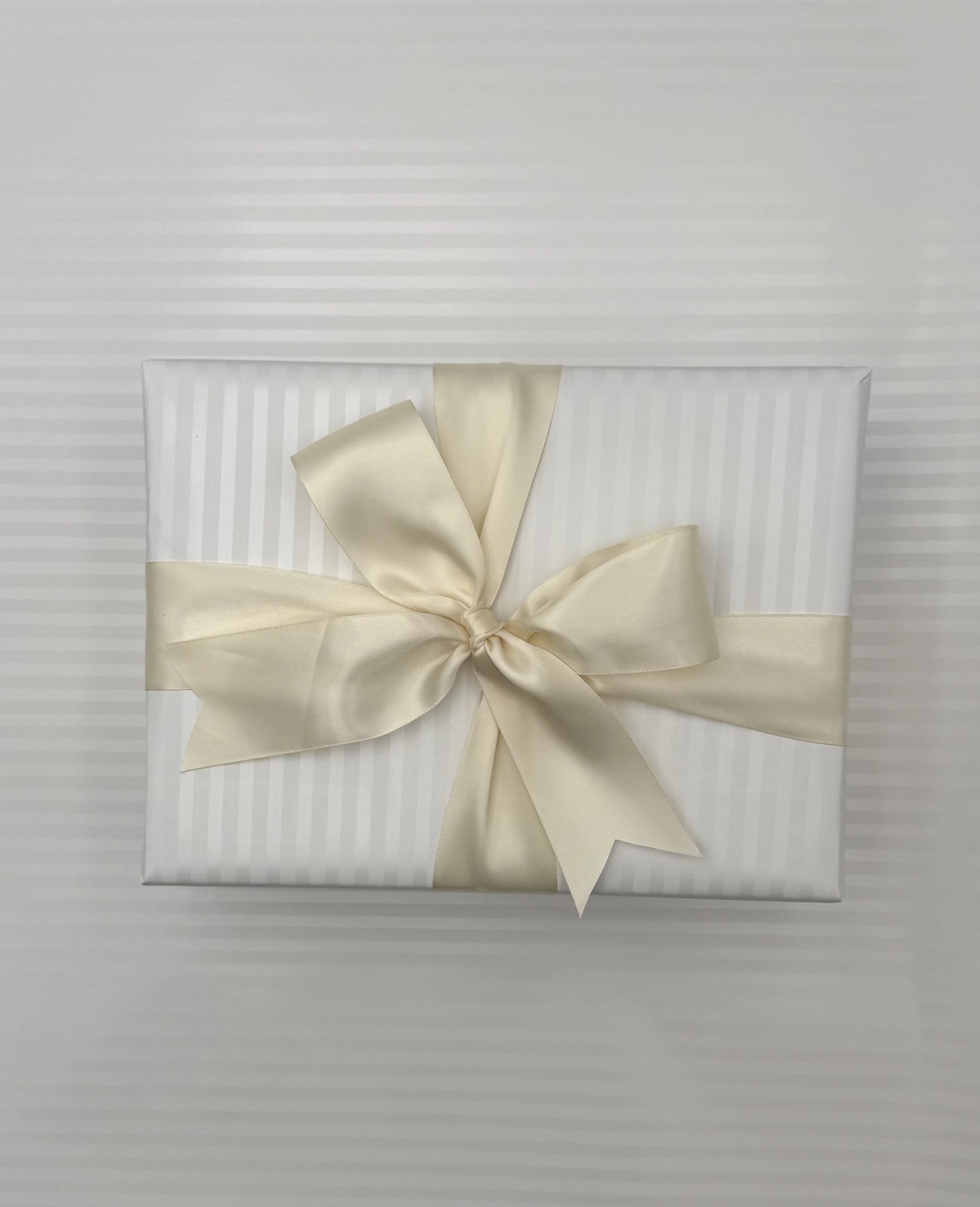 White gift box wrapped with a satin cream-colored ribbon tied in a bow.