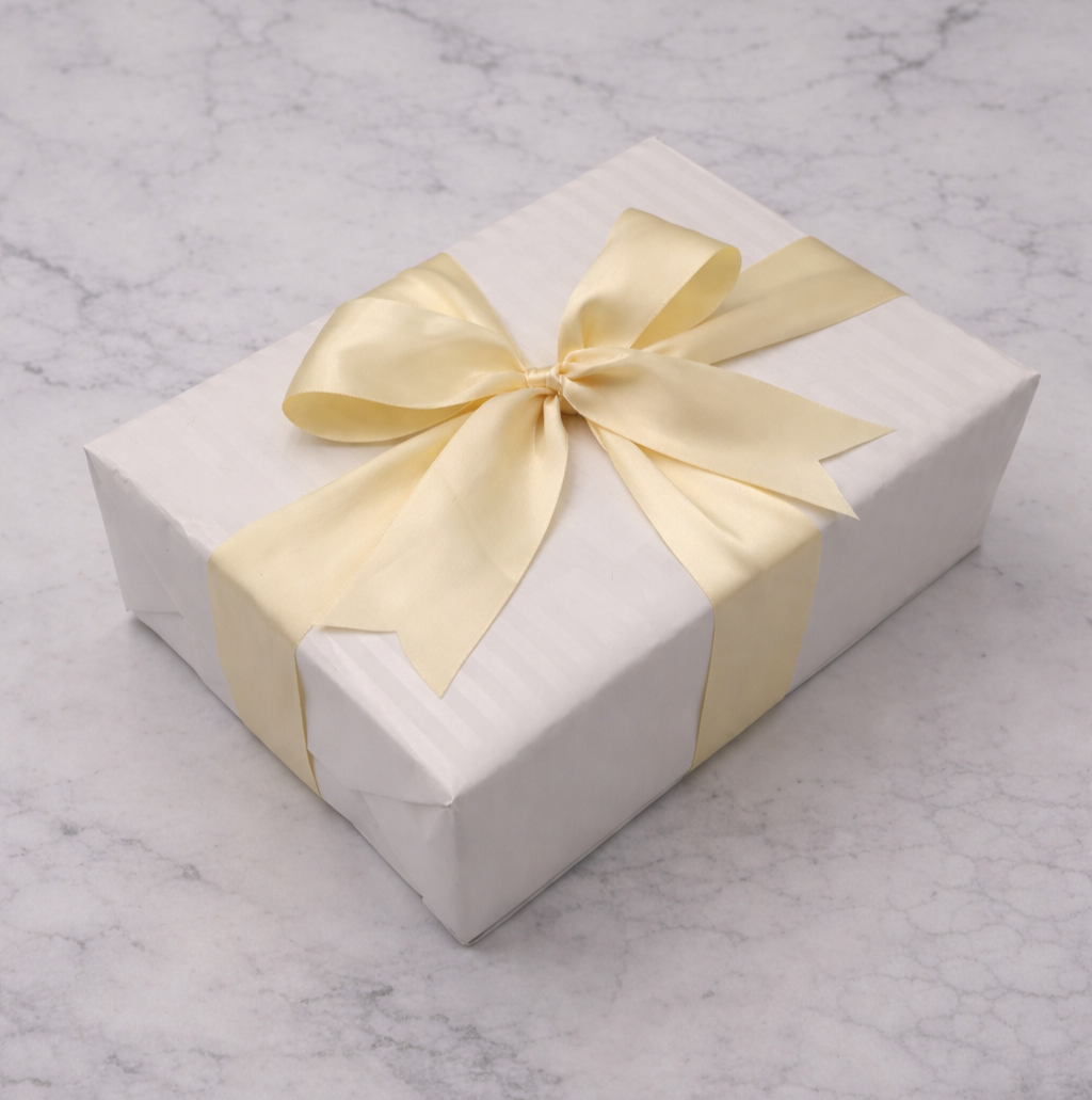 White gift box with a cream satin ribbon tied in a bow, placed on a marble surface.