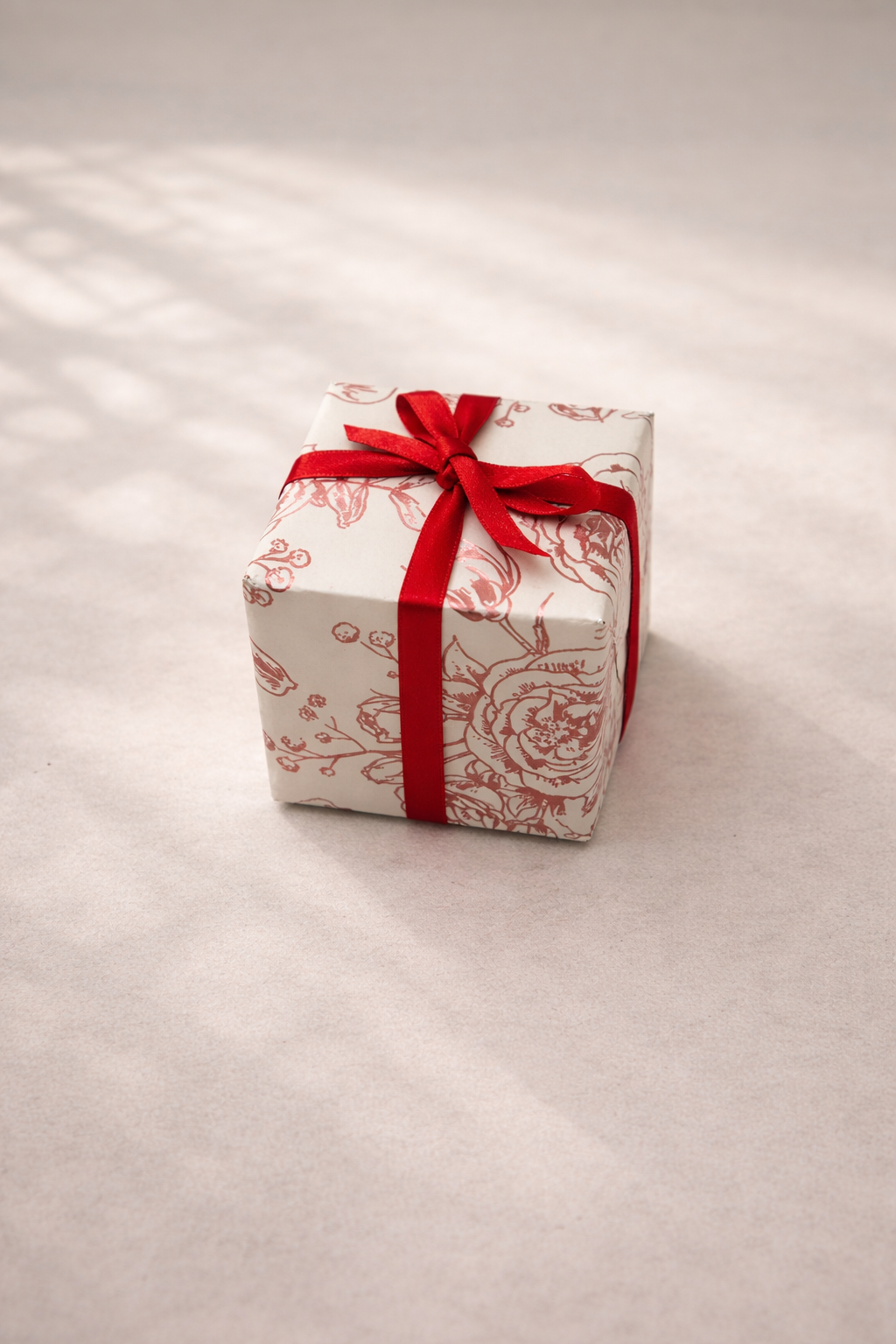Small gift box wrapped in floral-patterned paper with a red ribbon tied in a bow