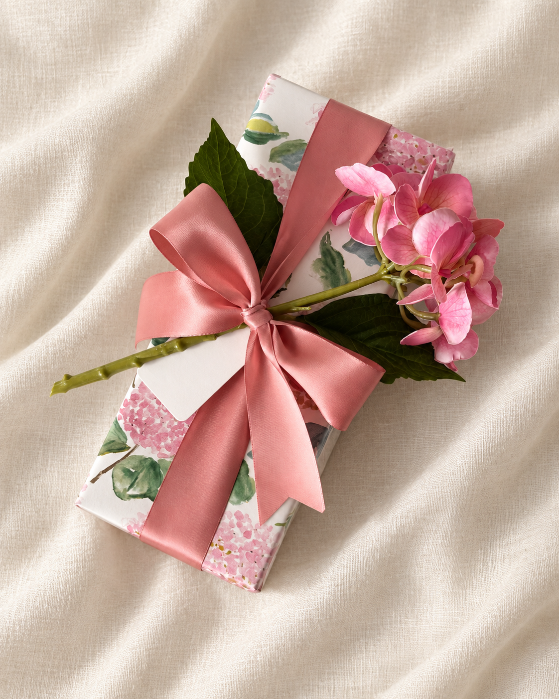 Pink floral gift with a pink bow beside pink flowers.