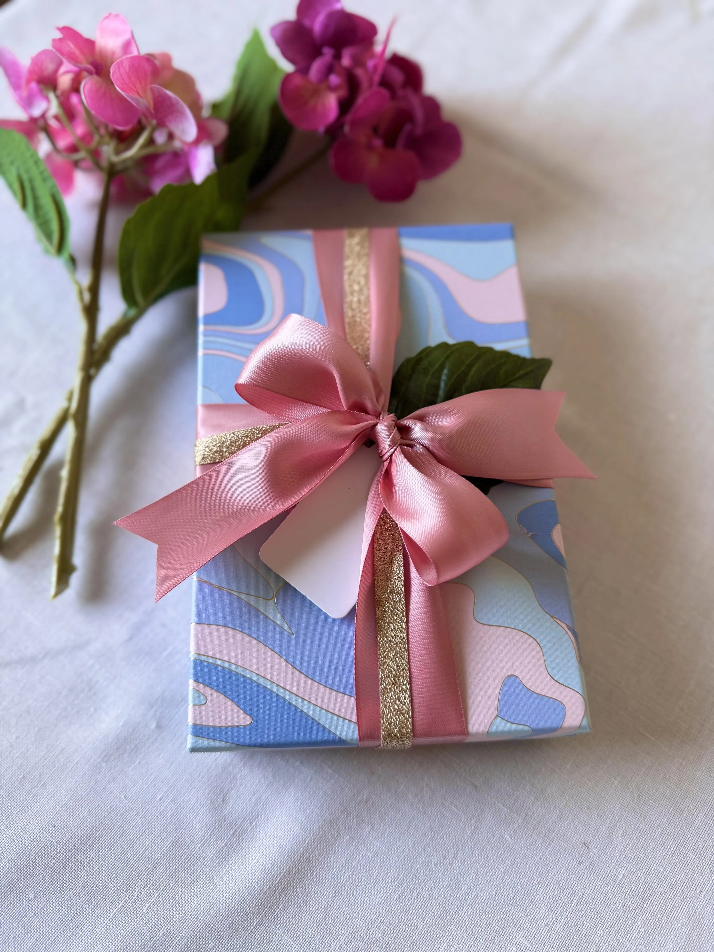 Blue and pink patterned gift with a pink bow beside pink flowers.