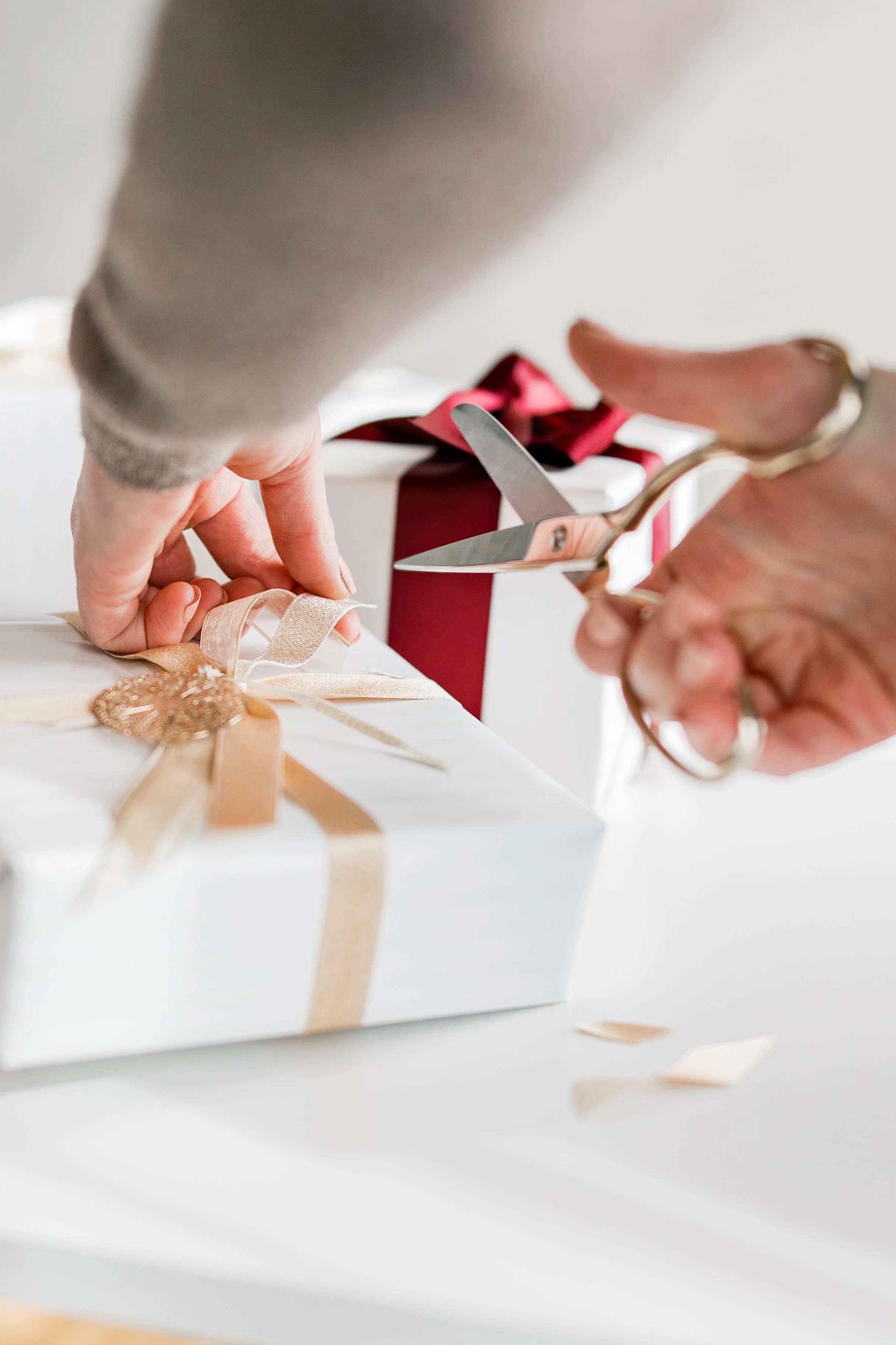 Hands trimming gold ribbon on a white gift box.