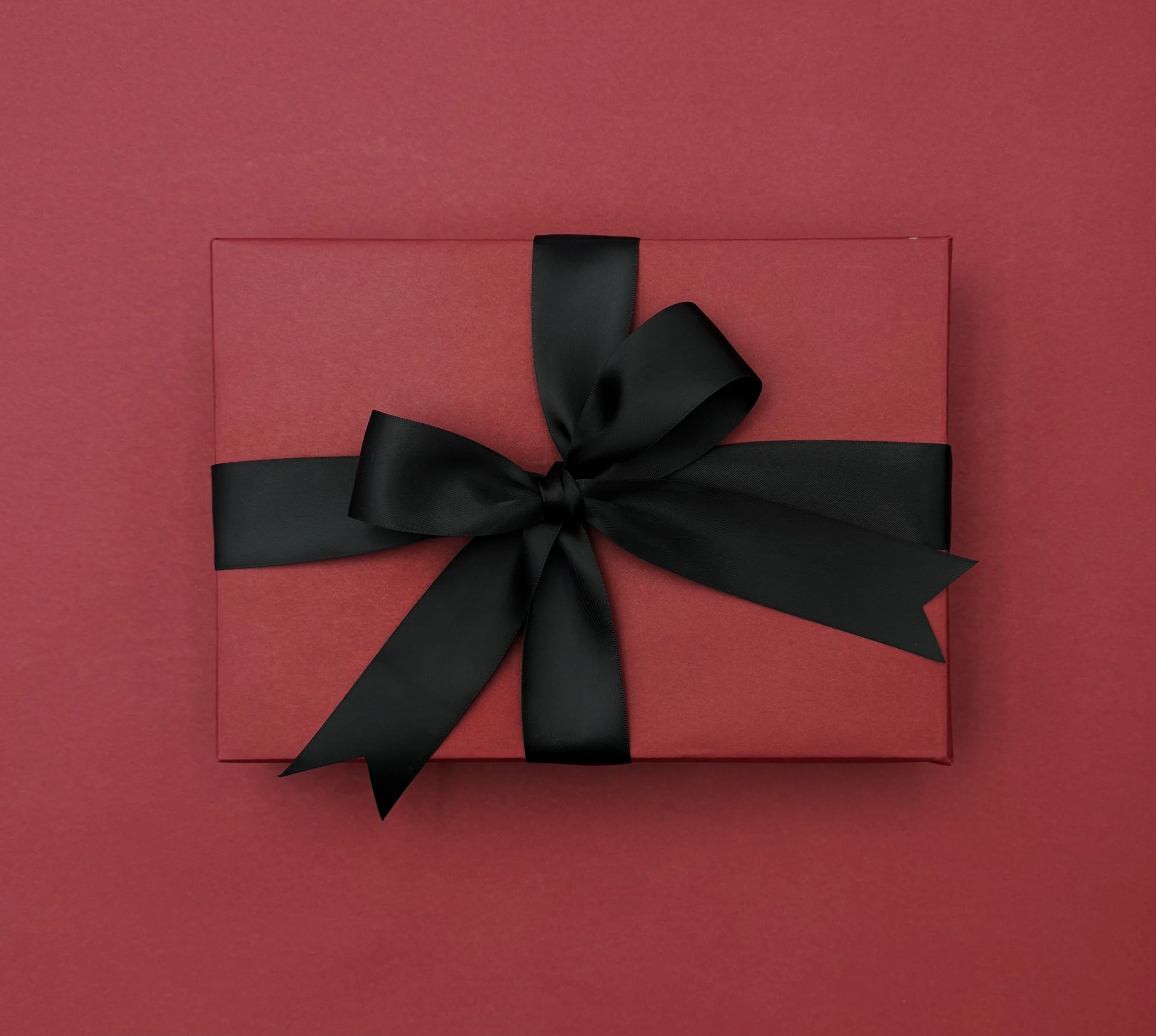 Red gift box wrapped with a black satin ribbon tied in a bow, on a red background.