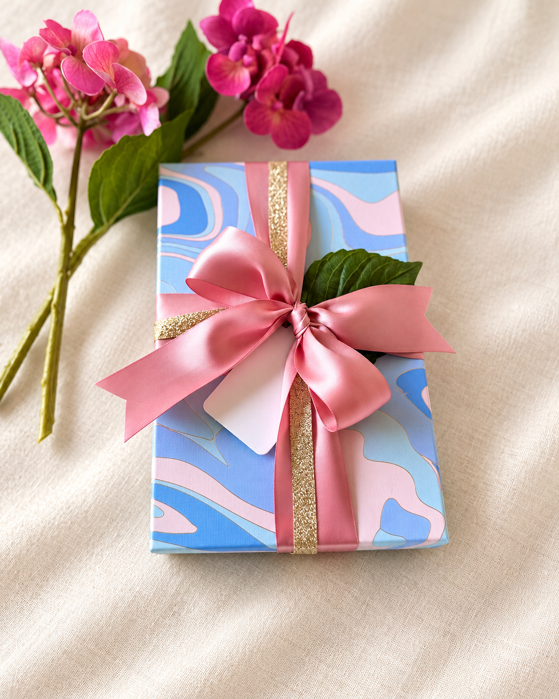 Blue and pink patterned gift with a pink bow beside pink flowers.